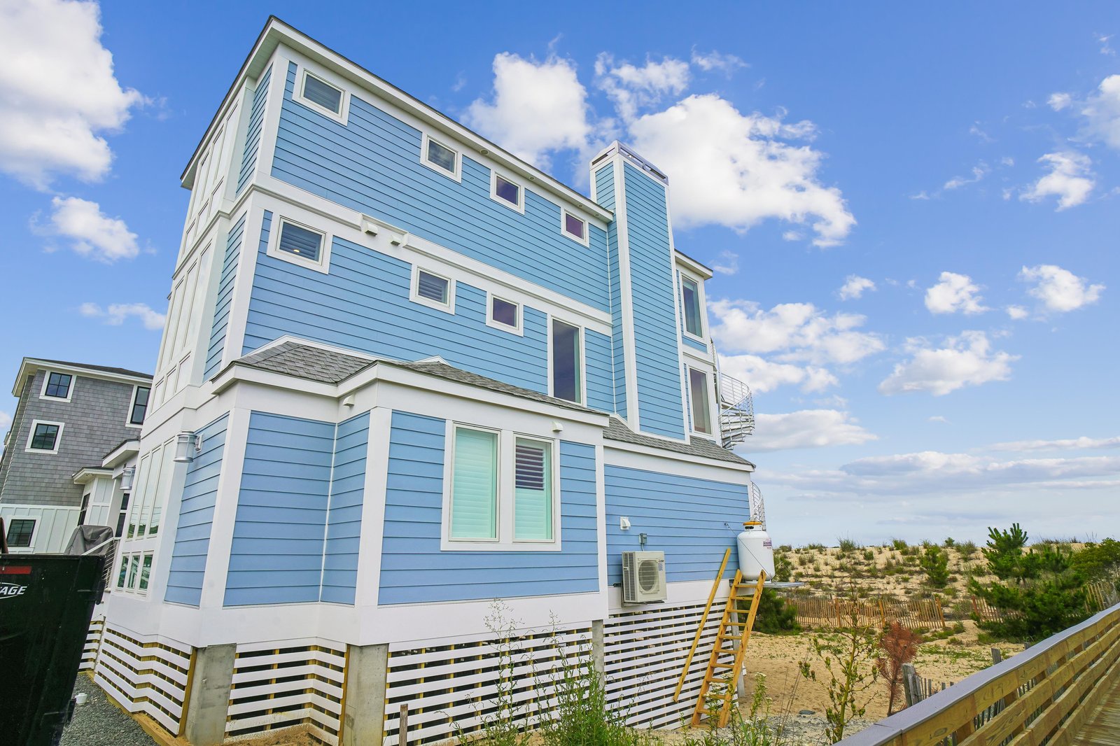 This bright blue coastal home features a modern exterior with ample windows and sits just steps from the sandy dunes of your private beach access.
