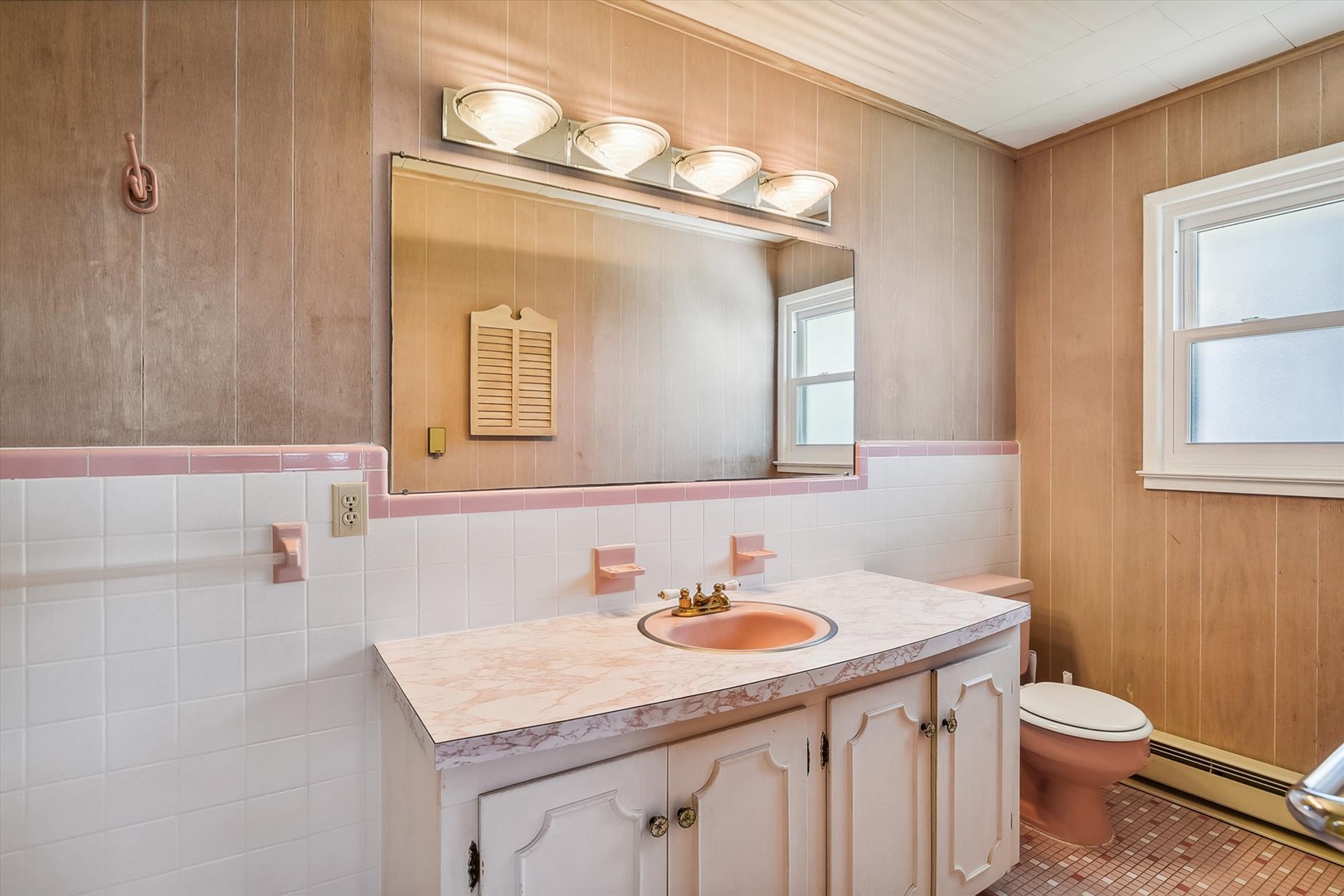 A charming vintage-style bathroom features a marble-topped vanity with classic fixtures, generous mirror with bright lighting, and retro pink accents that add personality to your private retreat.