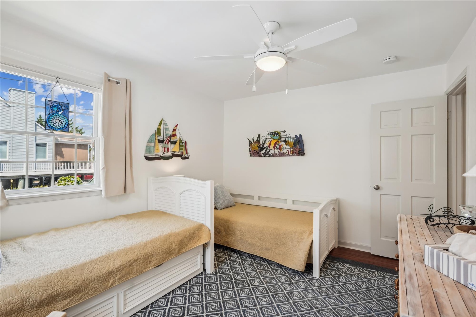 Two cozy twin beds await, perfect for friends or family sharing this bright coastal retreat. A ceiling fan keeps you cool while cheerful beach art adds playful charm.