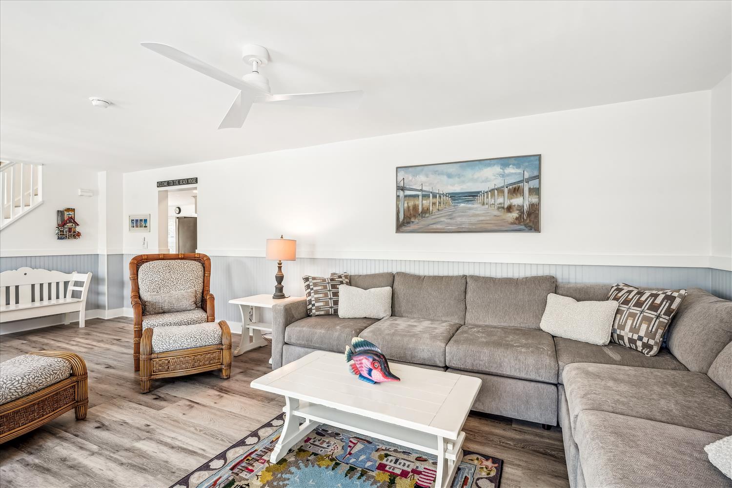 Unwind in your bright, coastal-inspired living room with plush sectional seating, beach-themed accents, and a ceiling fan for your comfort.