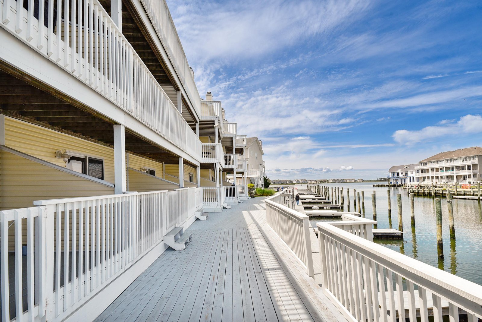 A spacious waterfront deck leads right to your private boat dock, with calm bay waters and coastal homes framing the view.