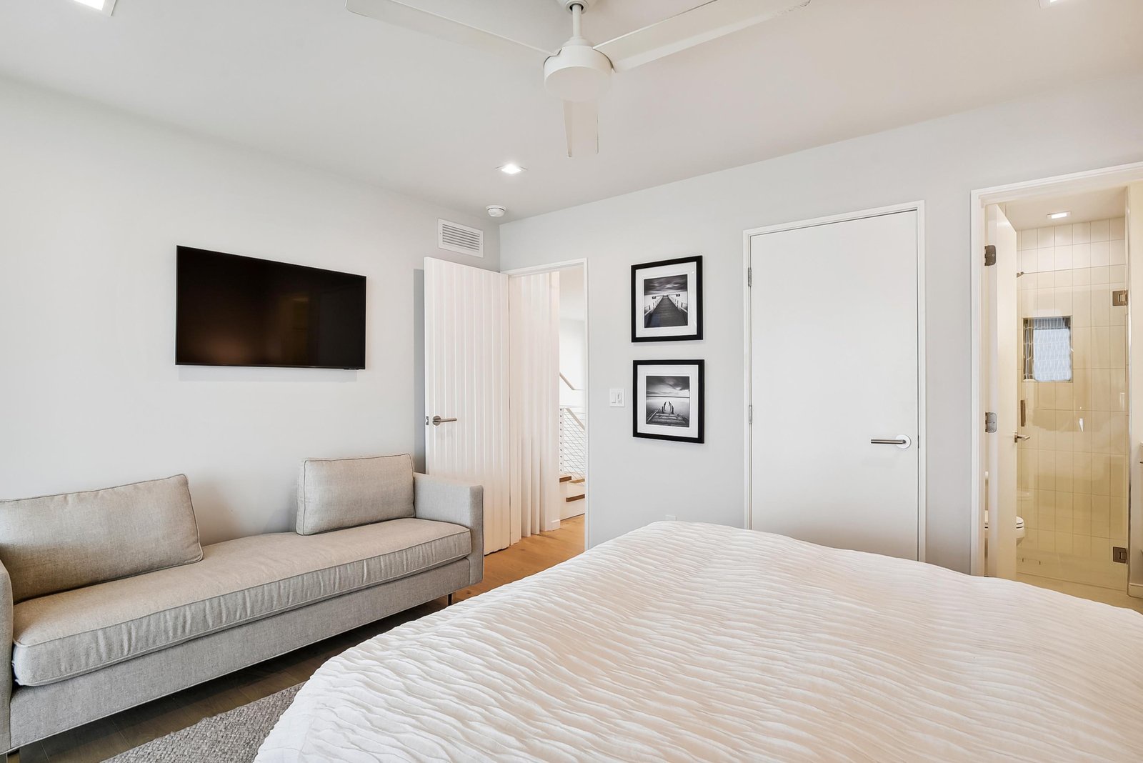 Your serene bedroom combines plush bedding with a cozy sofa for lounging, while the adjoining en-suite bath offers a sleek glass shower for refreshing mornings.