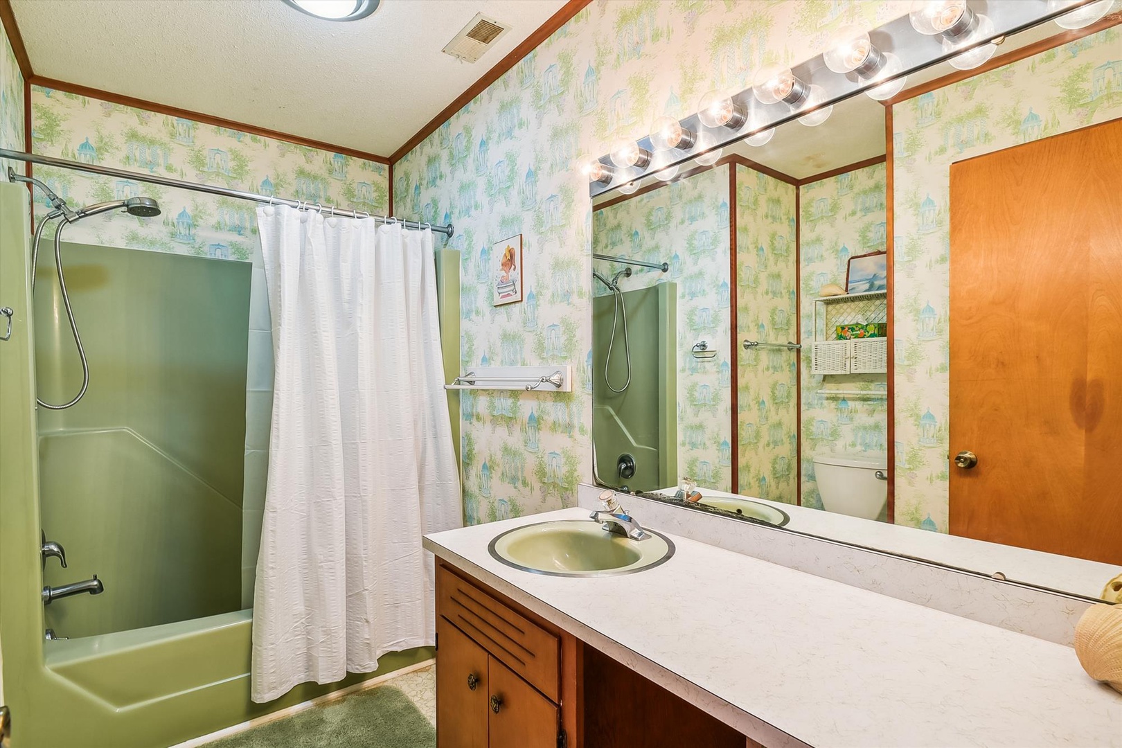 A bright bathroom awaits you with a spacious vanity, vintage-inspired wallpaper, and fresh towels, ready for your arrival and comfort.