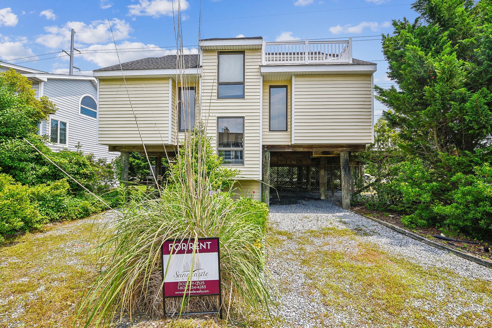 Beach retreat elevated on stilts with private parking and rooftop deck, nestled in a lush coastal neighborhood near the shore.