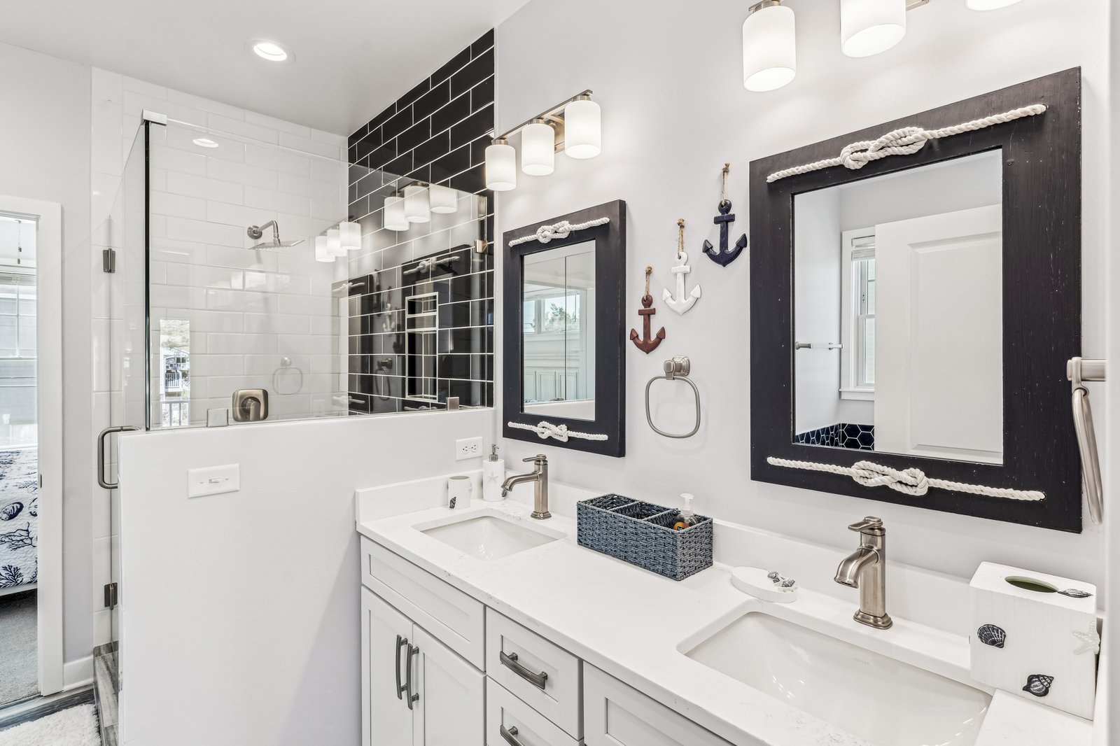 Your private bathroom blends crisp nautical style with modern comfort, featuring dual vanities, sleek black subway tile accents, and a spacious walk-in shower lit by bright pendant lighting.