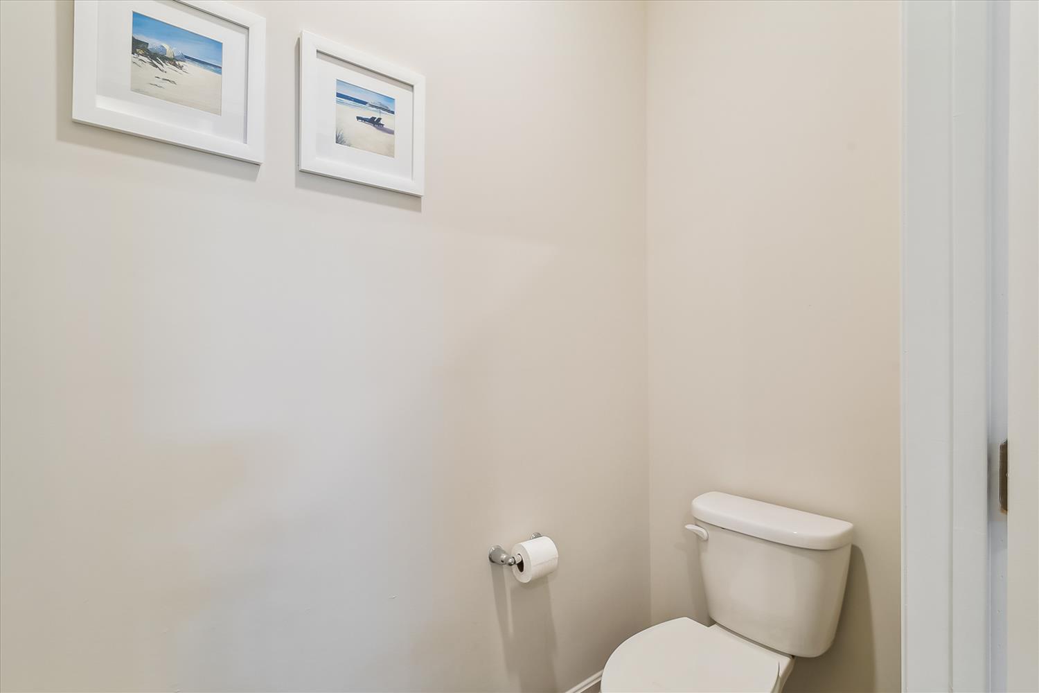 Your private powder room offers a clean, coastal-inspired retreat with serene beach artwork and crisp white finishes for your comfort.