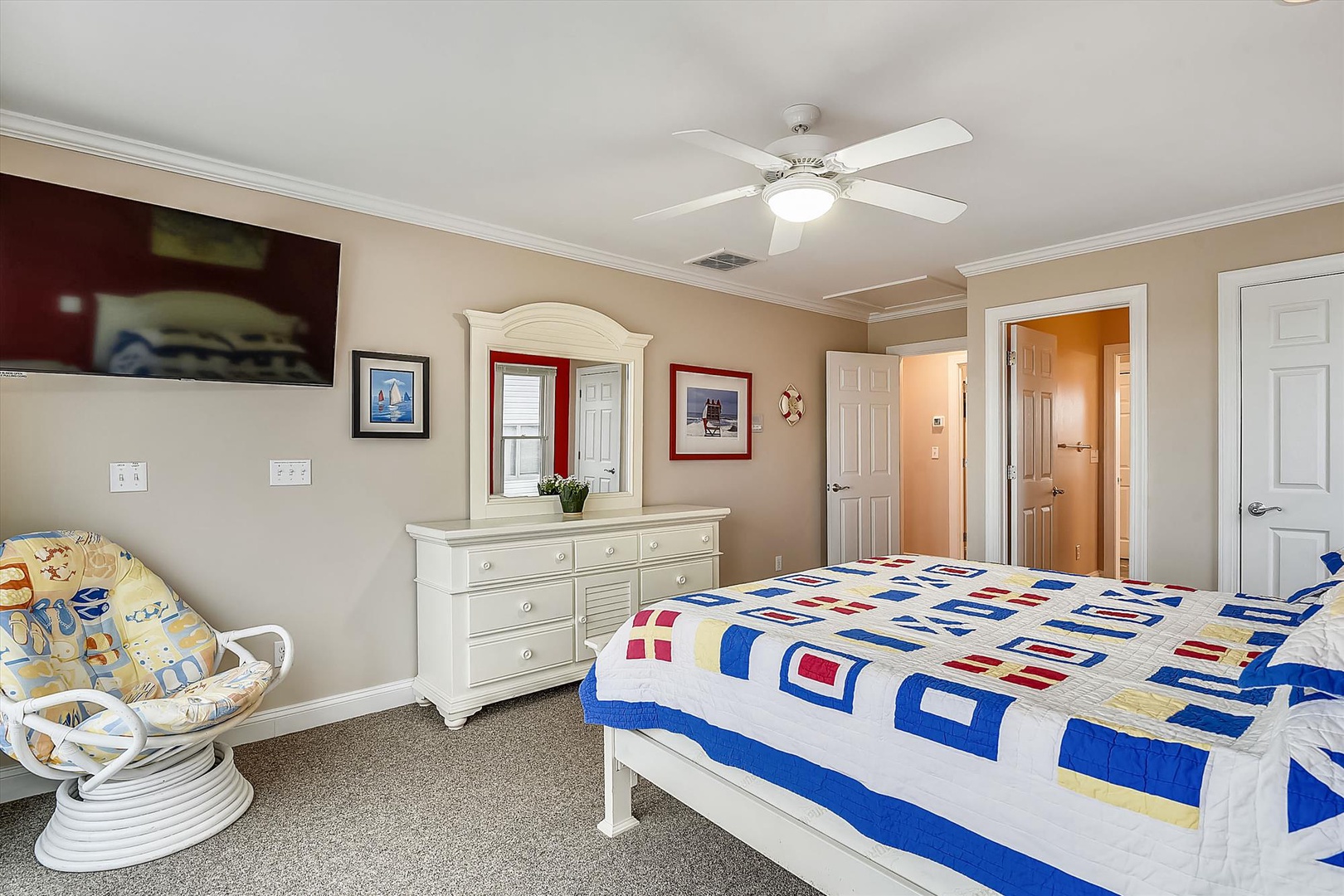 Drift off under a bright quilt with coastal breezes from the ceiling fan. This cheerful bedroom features a classic white dresser and cozy wicker chair—your seaside retreat awaits.