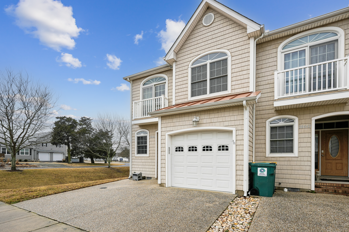 Two-story beige shingled townhome with white garage door and arched windows in residential neighborhood.