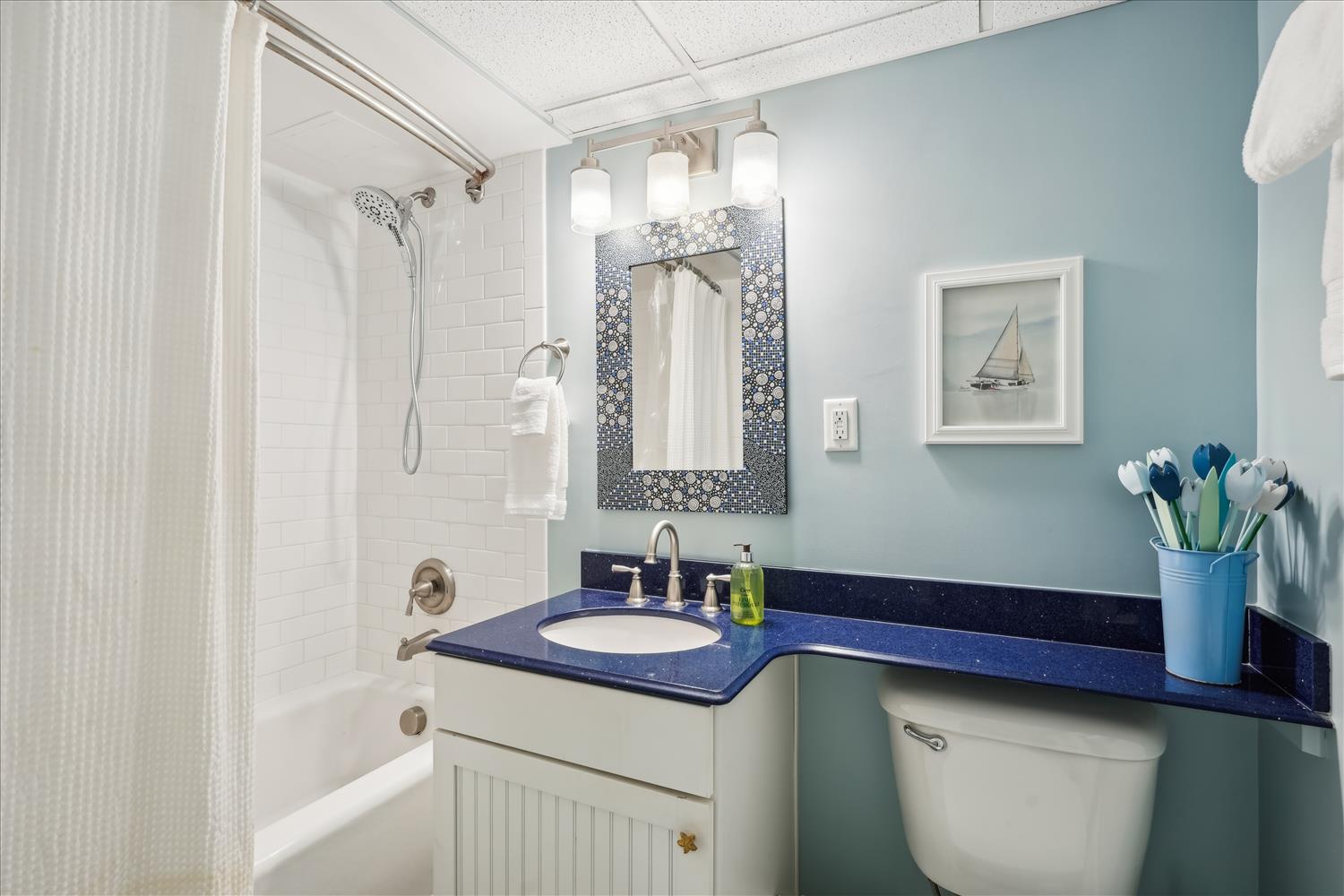 Refresh in your private bathroom with coastal charm—crisp white tile, soothing blue accents, and thoughtful touches like fresh flowers and artwork create a serene retreat after your day of adventure.