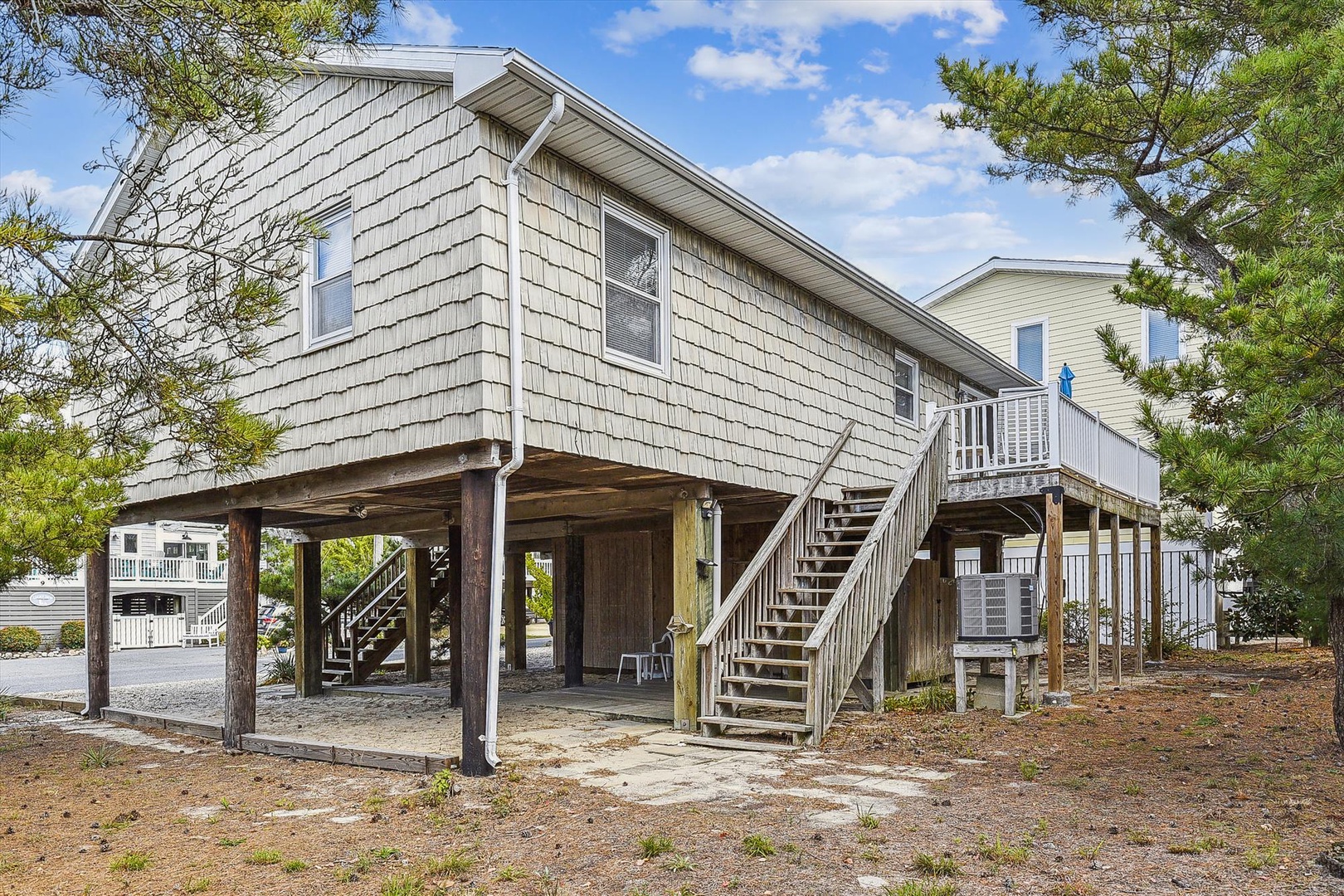 This elevated coastal home features sturdy construction on wooden pilings, offering secure parking underneath and a private entrance via the staircase. The property sits in a relaxed beach neighborhood.