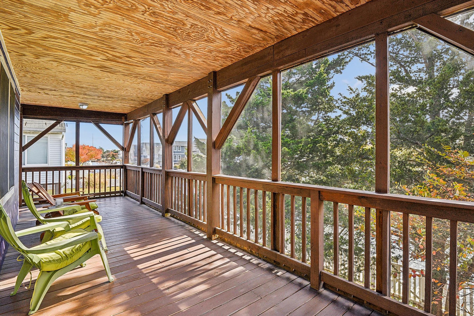 A covered porch with wood ceiling and railing overlooks nearby trees and homes, featuring seating for your outdoor relaxation.