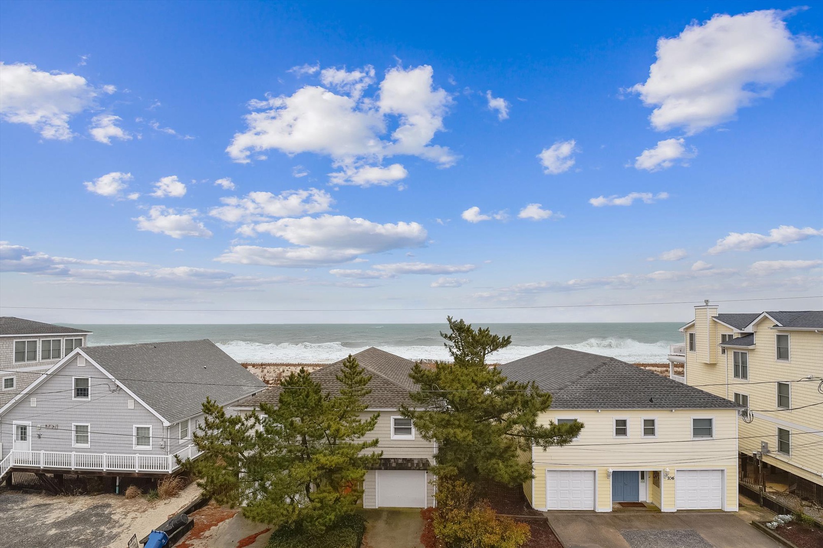 Coastal beach community with direct access to sandy shores and ocean waves, framed by neighboring beach houses and evergreen trees.
