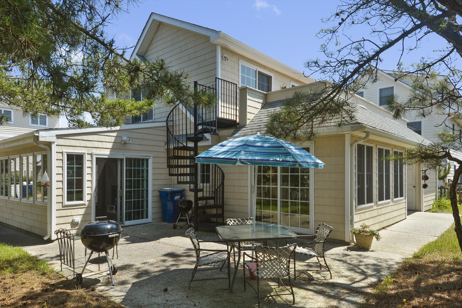 Your private outdoor dining area awaits, complete with a shaded table and BBQ grill, where you'll enjoy alfresco meals surrounded by coastal charm and dappled sunlight.