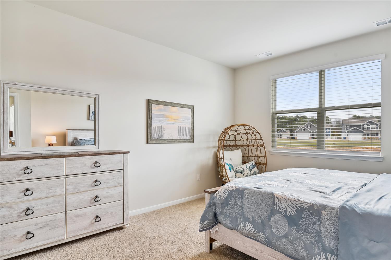 Your peaceful bedroom features coastal charm with a unique wicker chair, dresser storage, and bright windows overlooking the neighborhood.