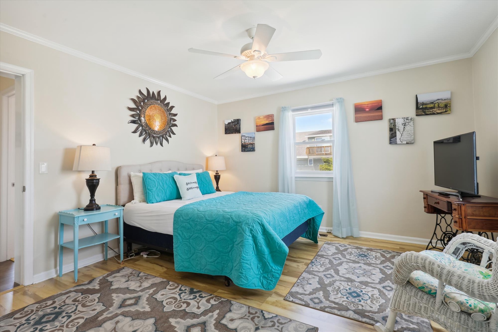 Step into your peaceful bedroom retreat with a plush bed dressed in vibrant turquoise, charming décor, a ceiling fan to keep you cool, and cheerful natural light—your perfect sanctuary for a restful stay.