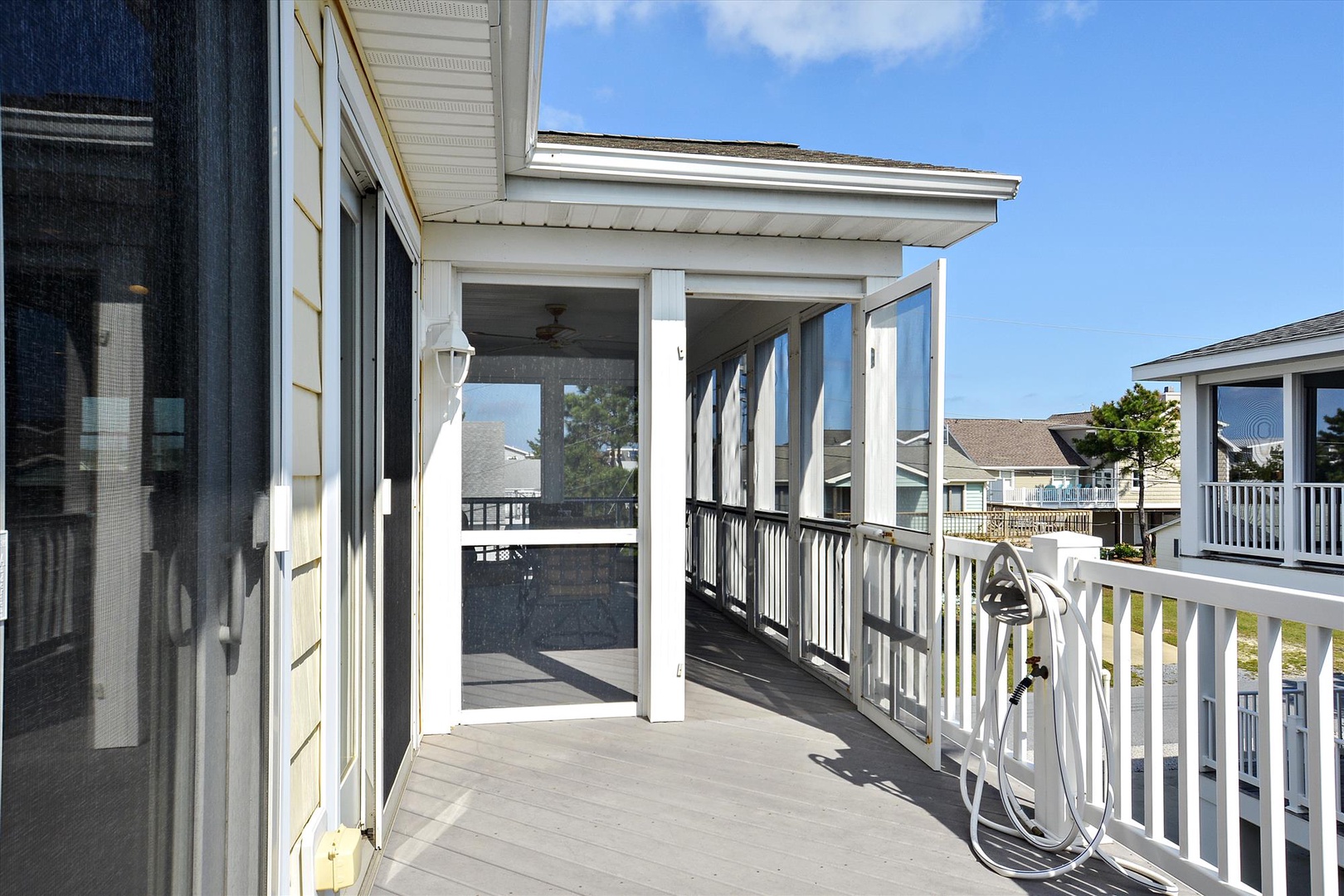 A spacious covered deck nestled in a quiet residential neighborhood, featuring a ceiling fan and clean white railings—perfect for morning coffee or evening relaxation.