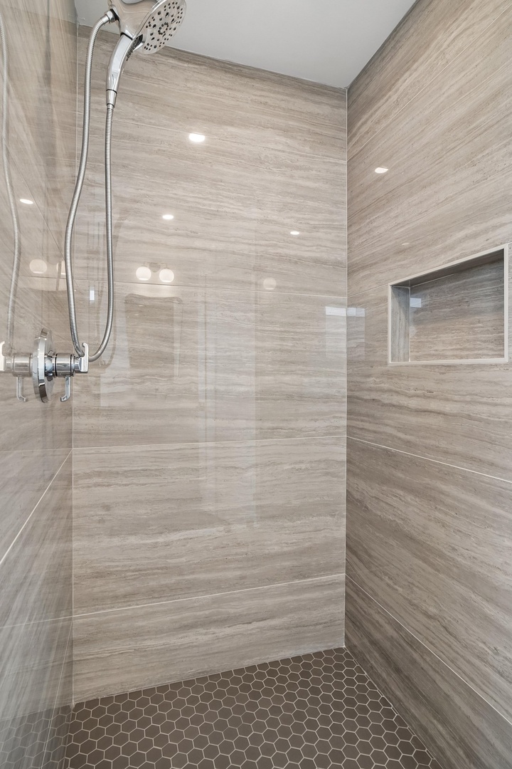 Rinse off the day in this beautifully tiled walk-in shower with a gleaming rainfall showerhead and handy built-in shelf for your essentials.