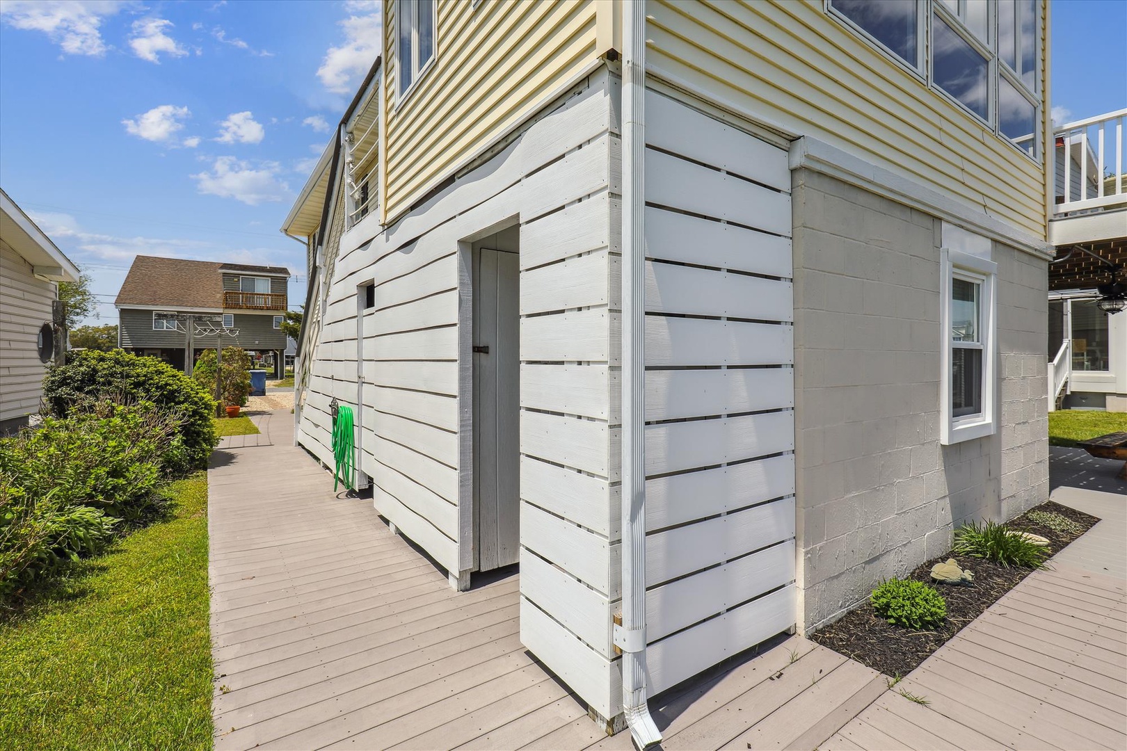 A coastal neighborhood with beach homes, wooden pathways, and outdoor storage for gear, all under a bright blue sky perfect for enjoying the seaside location.