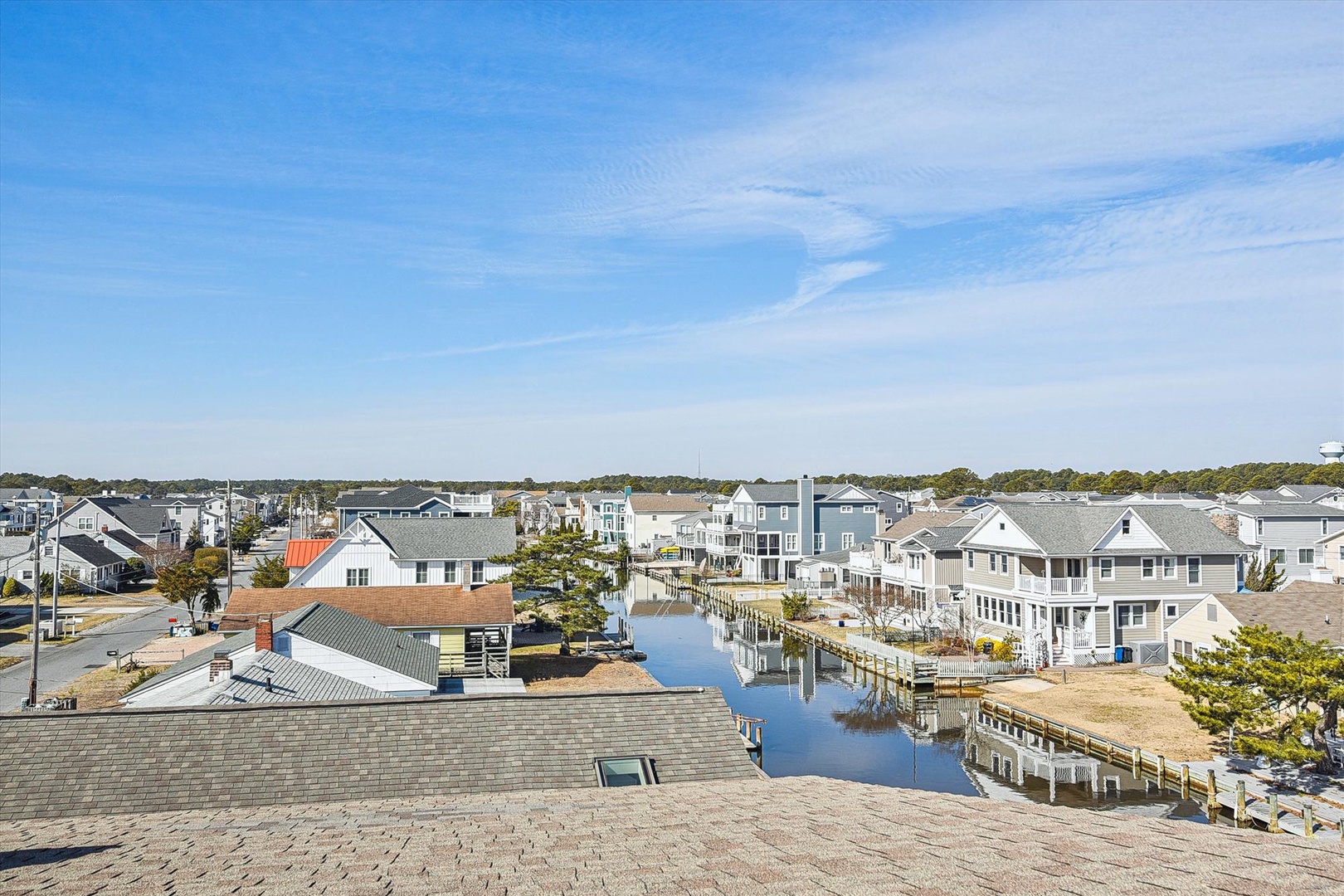 The property sits in a quiet waterfront neighborhood, with canal homes lining calm waters and a peaceful coastal community stretching toward the horizon.
