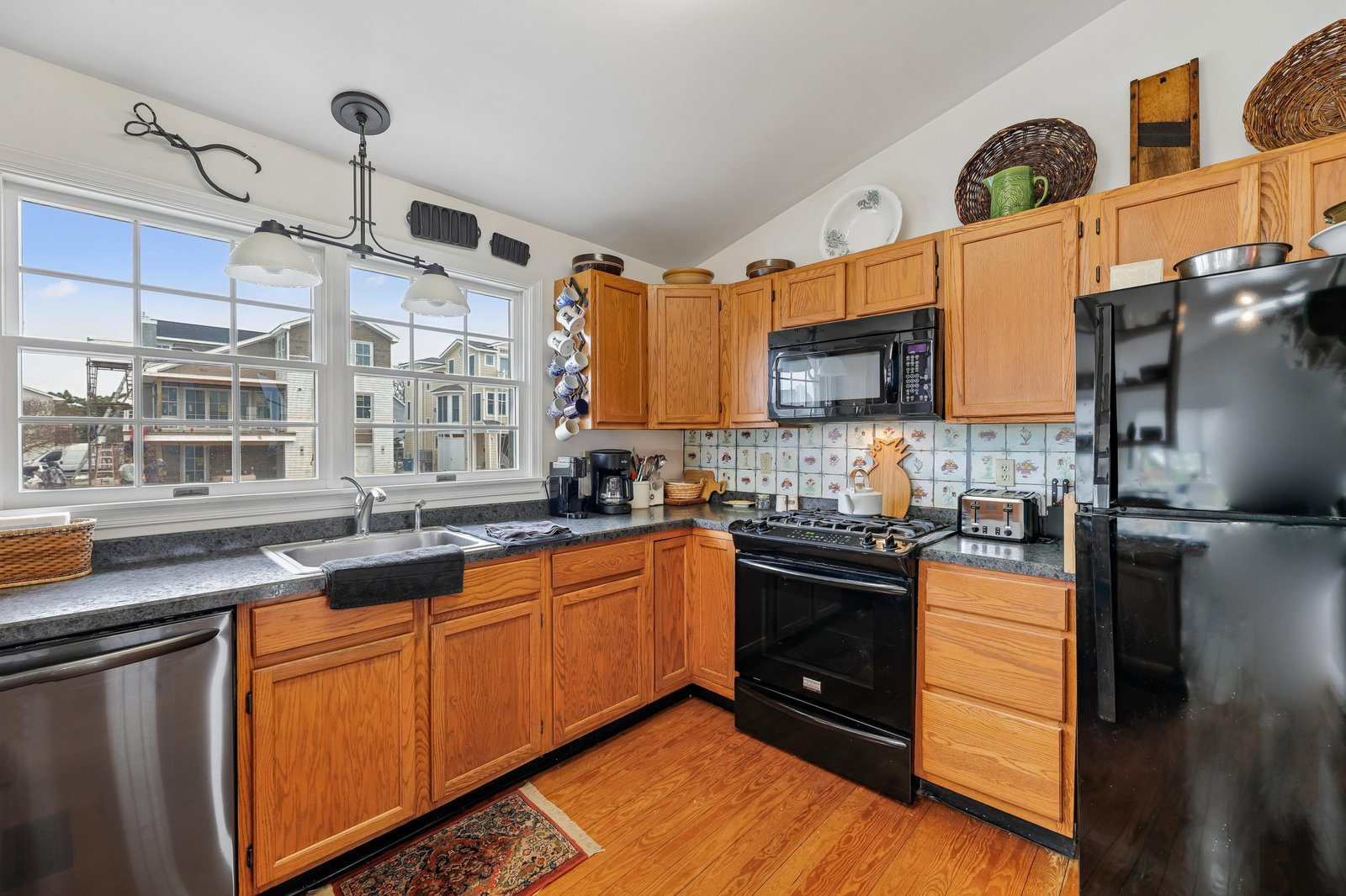 Your fully equipped kitchen features granite countertops, modern appliances, and warm wood cabinetry, perfect for preparing meals with natural light streaming through large windows.