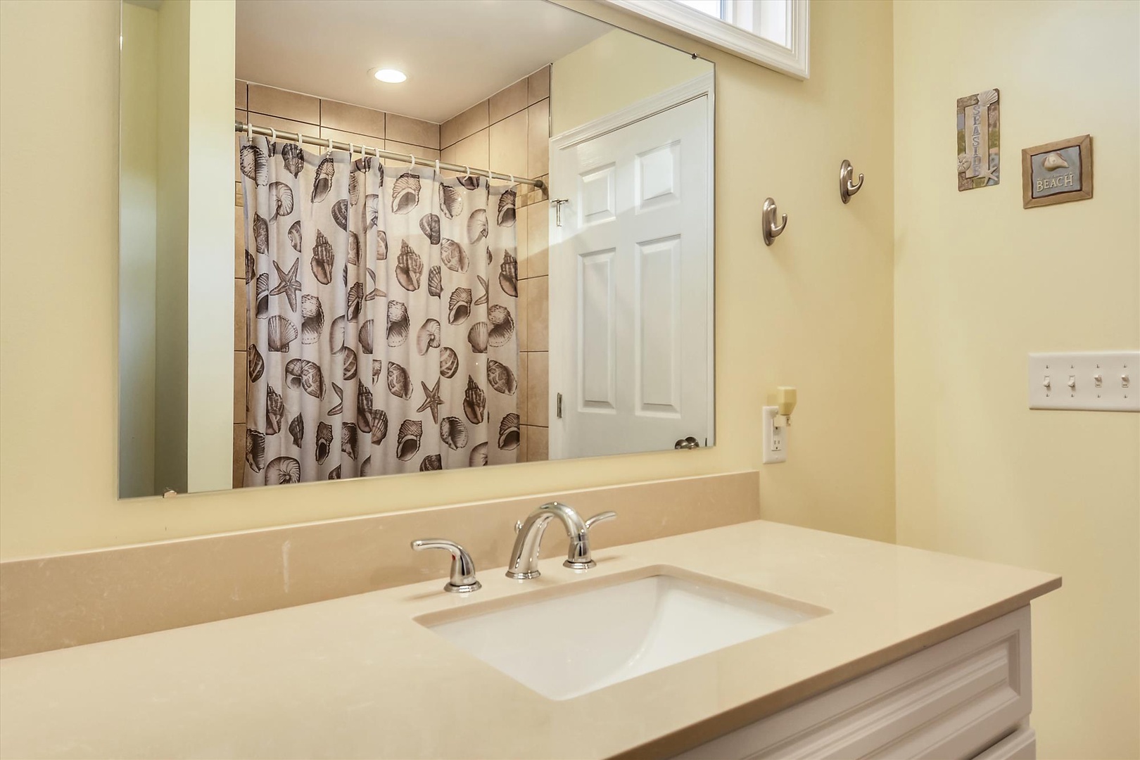 Step into your bright bathroom with a spacious sink and beach-themed touches. The tiled shower behind will refresh you after sunny days exploring the coast.