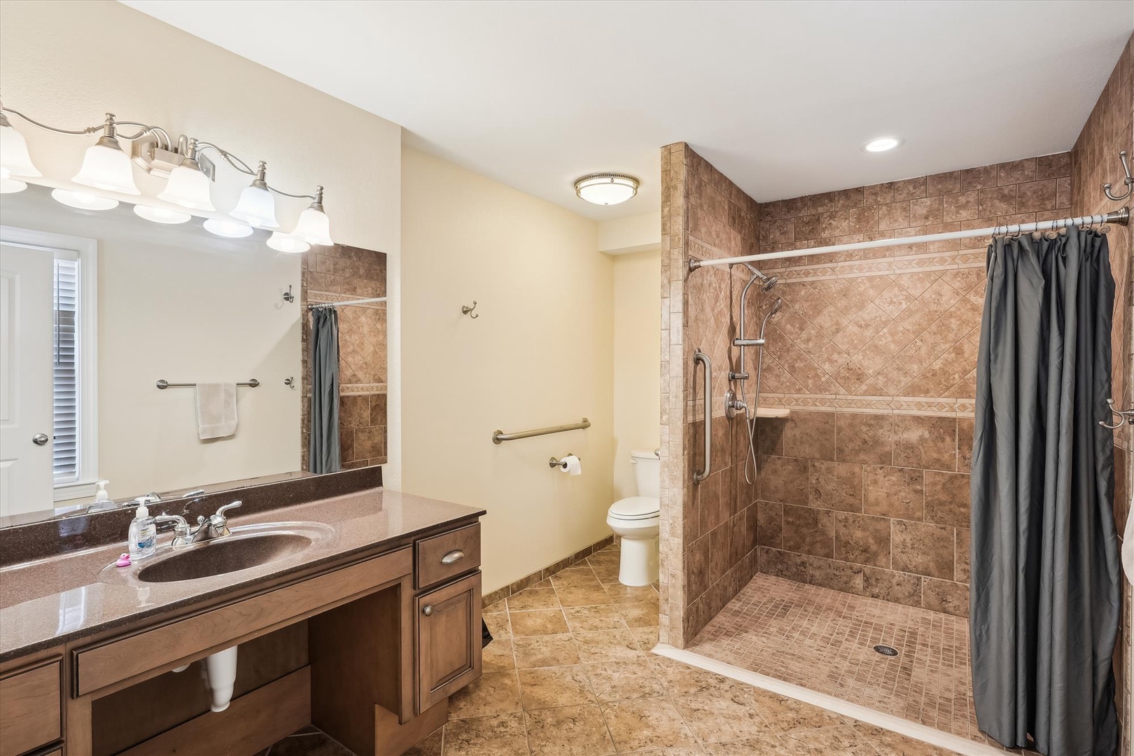 Your spacious bathroom features warm tile and accessible design with grab bars throughout. Enjoy the walk-in shower and generous vanity space as you freshen up for the day.