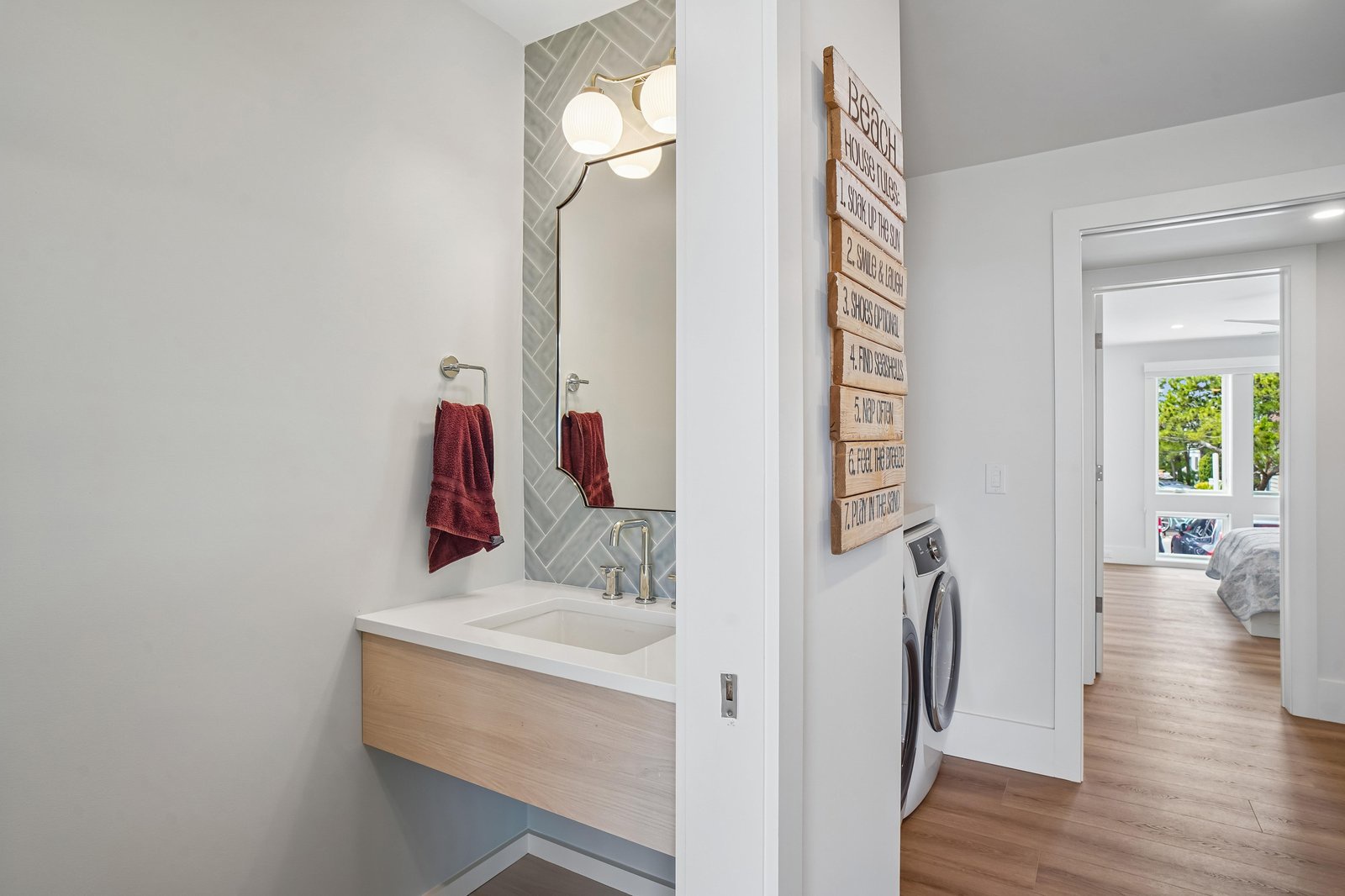 A chic bathroom and laundry nook blend convenience with modern style. The sleek vanity, herringbone tile accent, and fresh white finishes create a bright, inviting space for your daily routine.