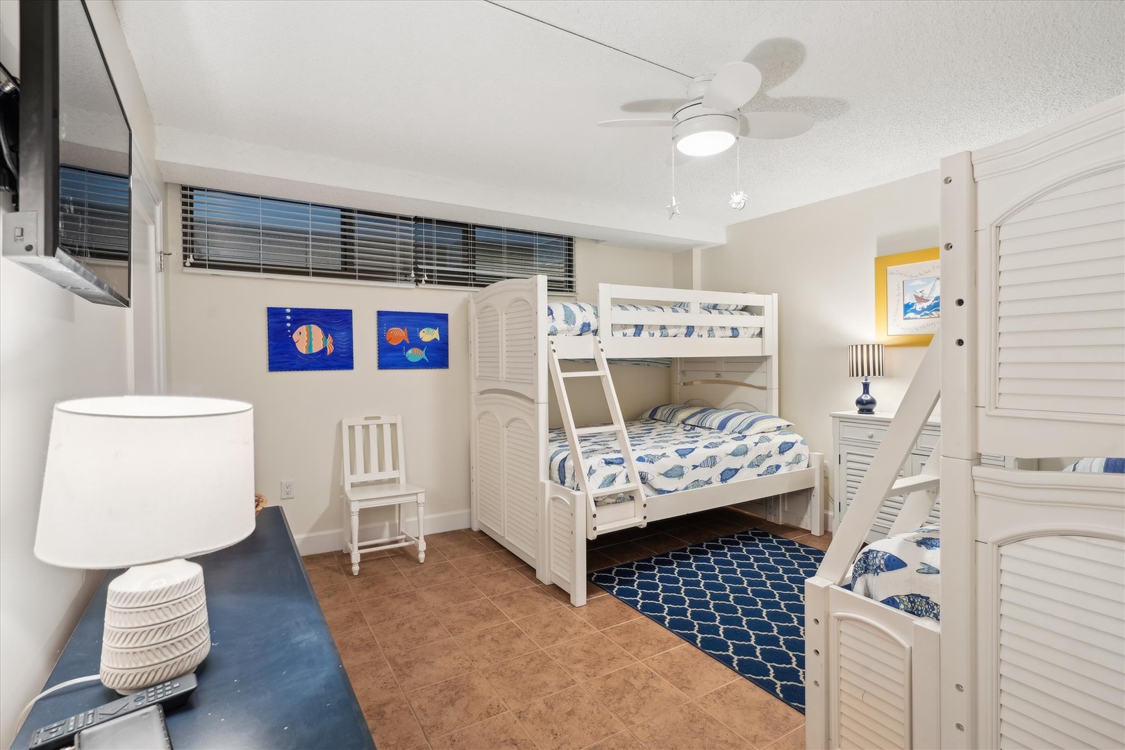 Your kids will love this ocean-themed bunk room with white beds, playful fish art, and a cozy coastal vibe perfect for family adventures.