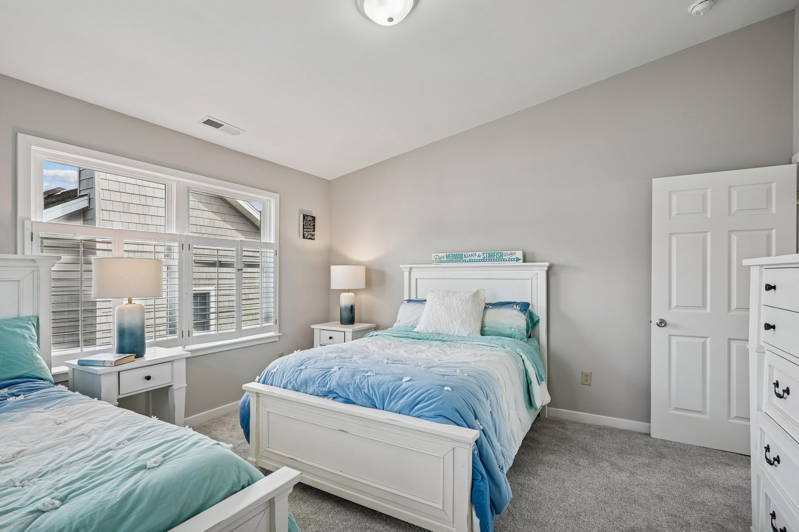 Your peaceful retreat features comfortable twin beds with coastal-inspired linens, crisp white furniture, and soft natural light filtering through plantation shutters—perfect for restful mornings.