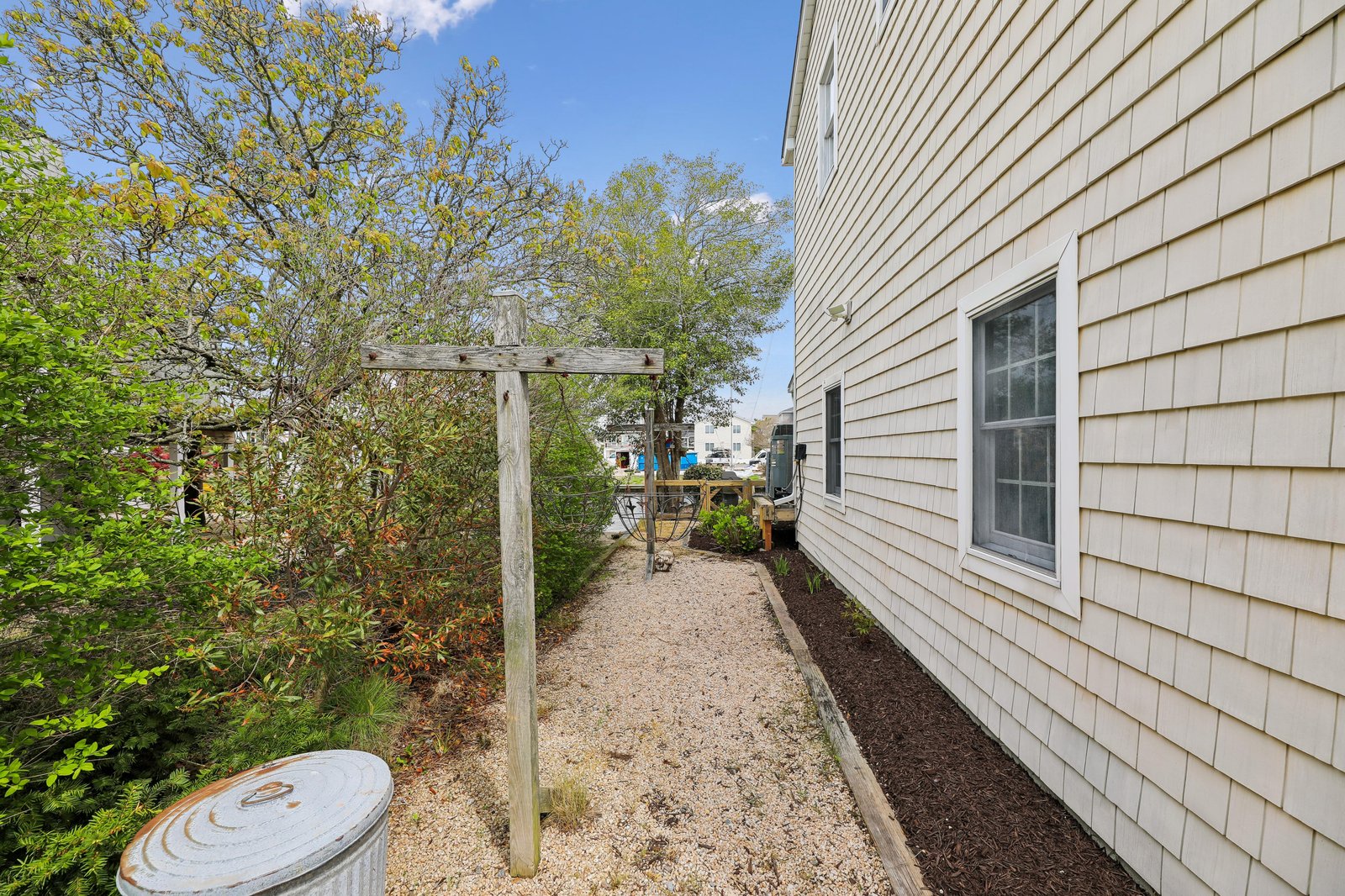 The property features a charming gravel pathway framed by lush greenery and a simple wooden arbor, leading to the outdoor spaces and surrounding neighborhood. Perfect for morning strolls or sunny afternoon exploration.