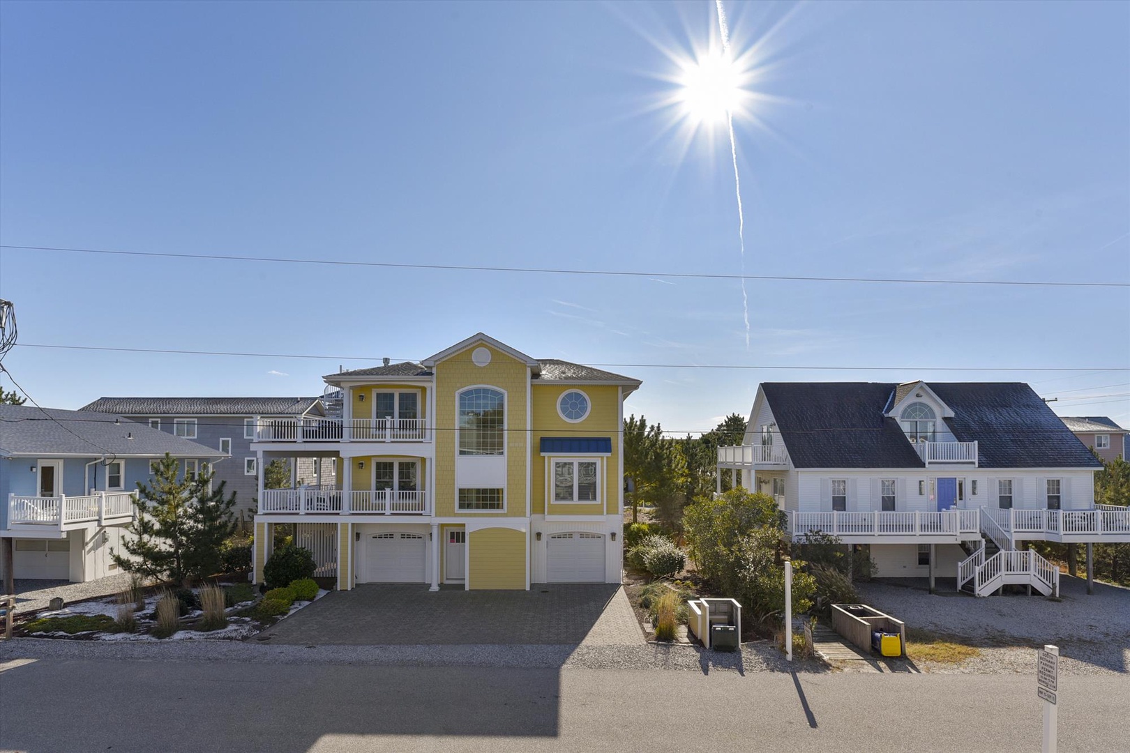 This distinctive yellow beach house stands out in a quiet coastal neighborhood, surrounded by similar vacation homes and featuring ample parking space, perfect for family getaways.