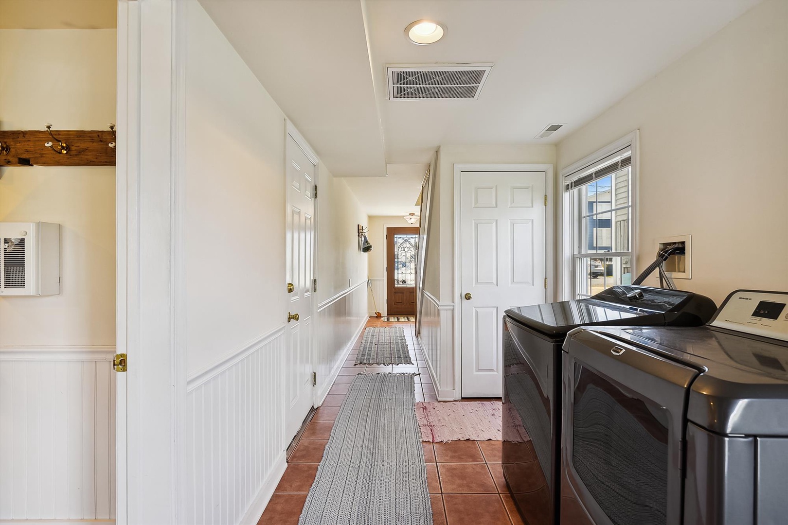 Step into your bright, welcoming hallway with convenient laundry facilities right at hand. The warm terra-cotta tiles and crisp white paneling create a fresh, inviting space where you'll appreciate the home's thoughtful details.
