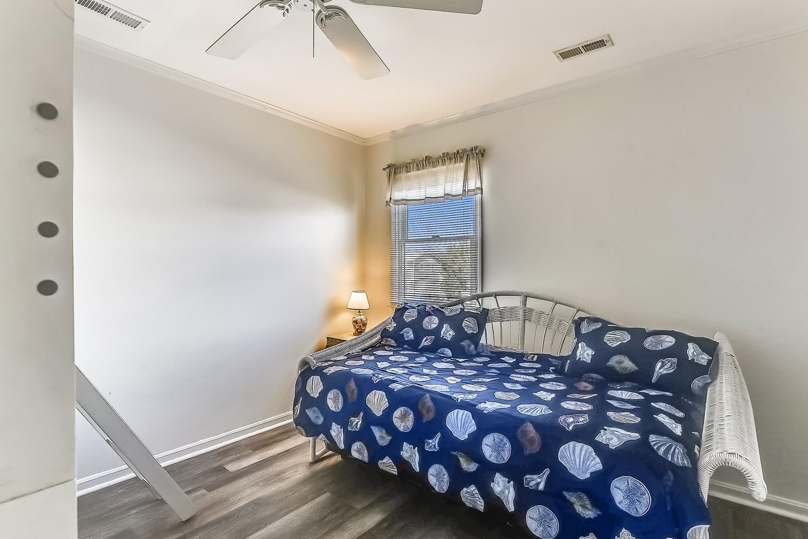 Slip into this serene coastal bedroom where soft light filters through the window and a gentle ceiling fan stirs the air. Your restful retreat awaits with beachy charm and comfort.