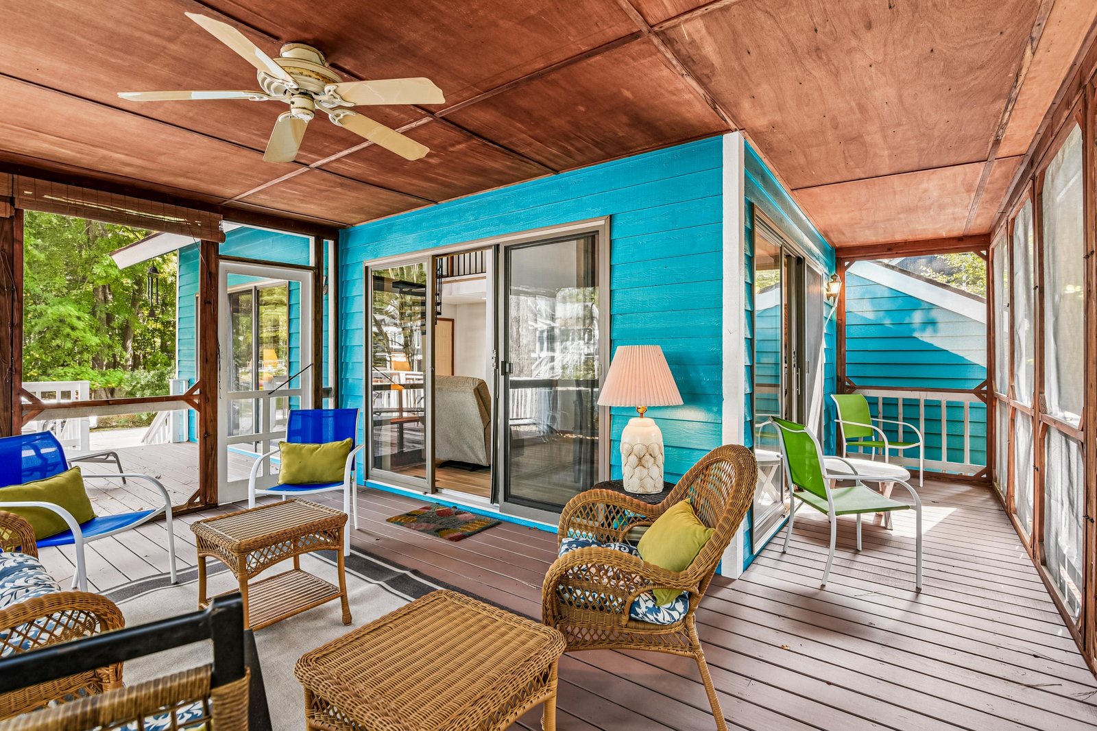 Step onto your screened-in porch, where wicker seating invites you to relax under a warm wood ceiling, surrounded by vibrant turquoise walls and views of lush greenery just beyond the windows.
