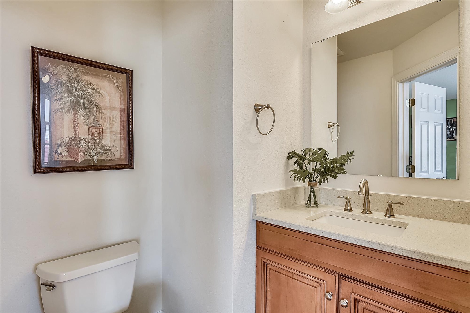 Step into your elegant half-bathroom featuring warm wood cabinetry, polished countertops, and tropical artwork that creates a welcoming retreat.