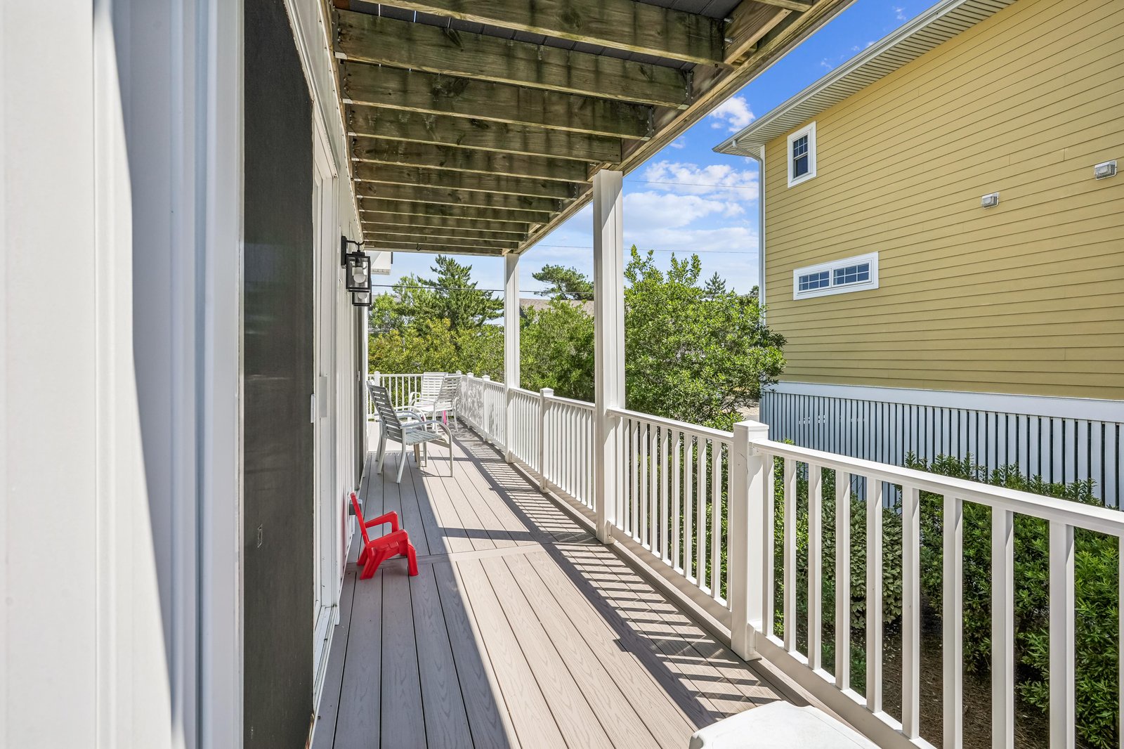 A covered balcony with seating overlooks the neighborhood, offering a peaceful spot to enjoy fresh air and blue skies on sunny summer days.
