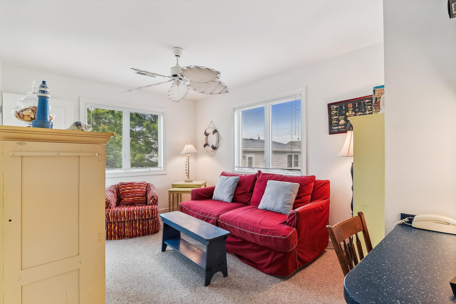 Sink into the plush red sofa and feel the ocean breeze from your ceiling fan as natural light fills your cozy coastal retreat—perfect for unwinding after beach adventures.