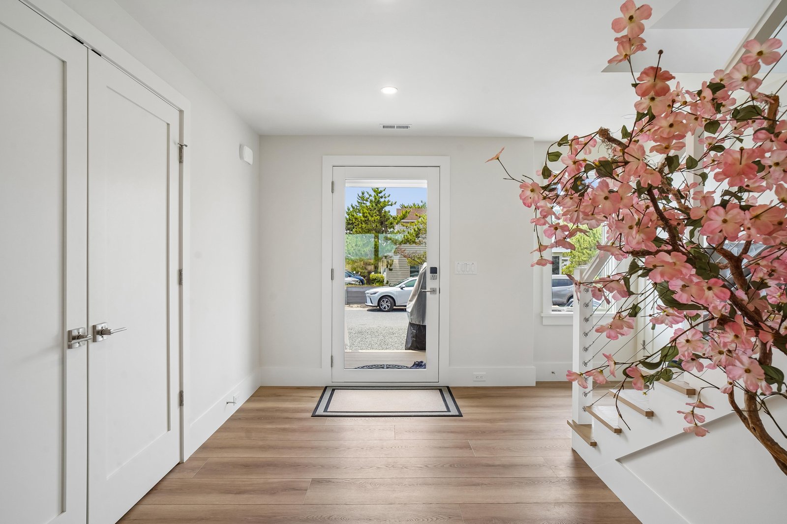 A modern entryway featuring warm wood floors, crisp white walls, and decorative pink blossoms sets a welcoming tone from the moment you arrive at the property.