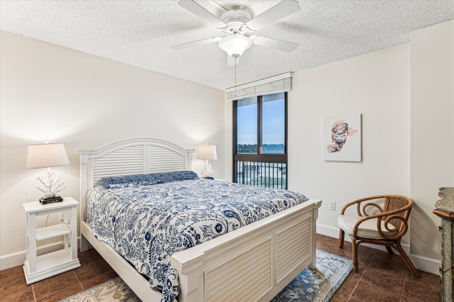 Wake up to serene waterfront views right from your bed. The ceiling fan keeps you cool while coastal breezes drift through, and those blue-and-white linens echo the peaceful water just beyond your window.