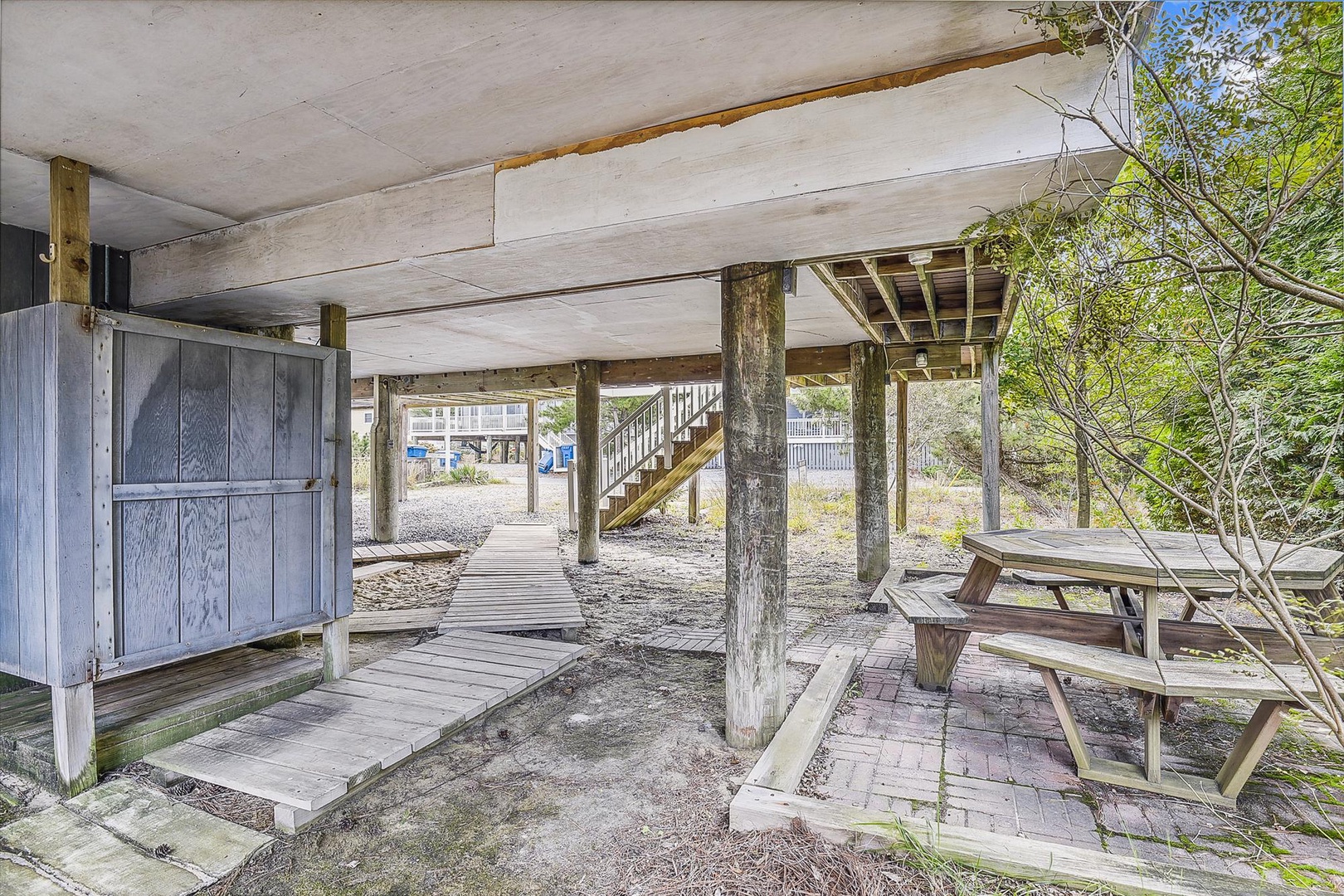 Covered ground-level area beneath the elevated property offers sheltered outdoor storage and shaded space near the beach access walkway.