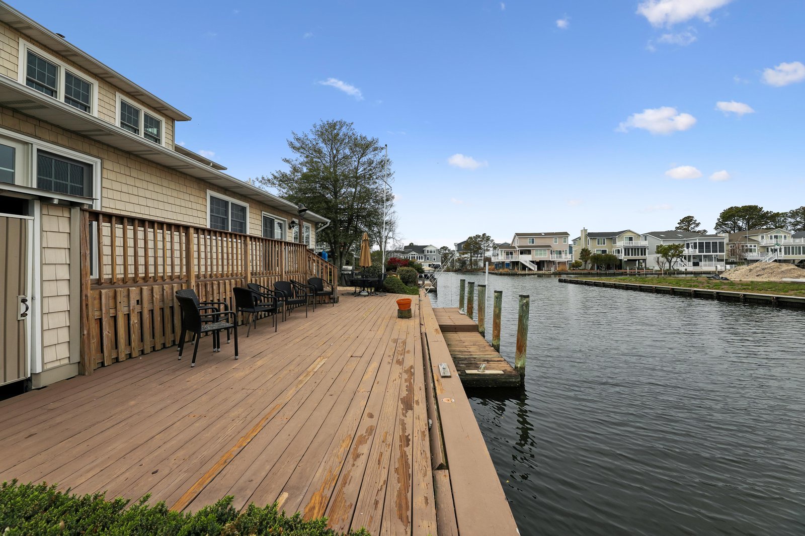 A waterfront home features a spacious wooden deck overlooking a peaceful canal, offering direct water access and views of the surrounding residential community.