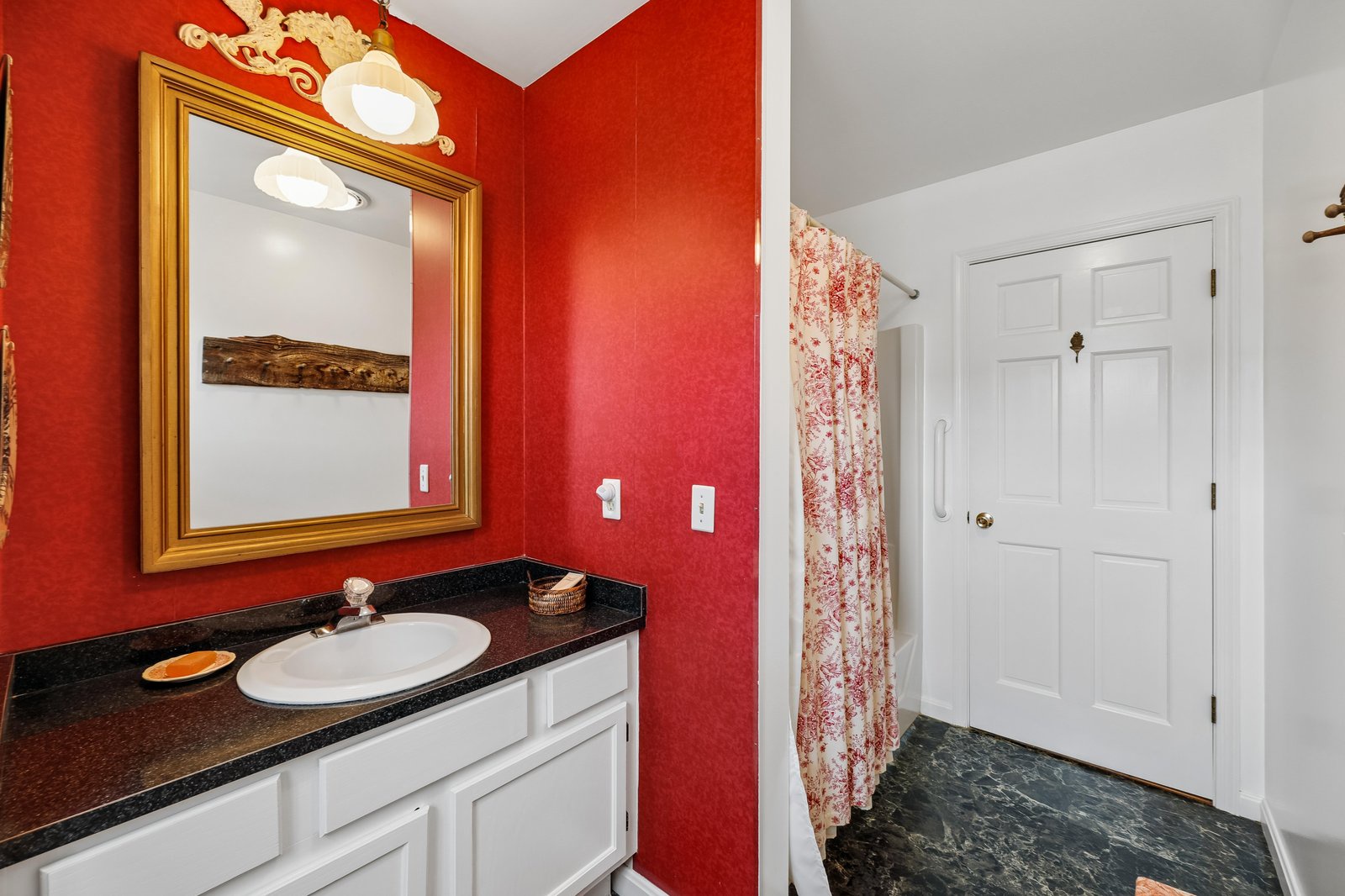 Step into your private bathroom with striking red walls, a polished black countertop, and elegant golden accents that make every moment feel special.
