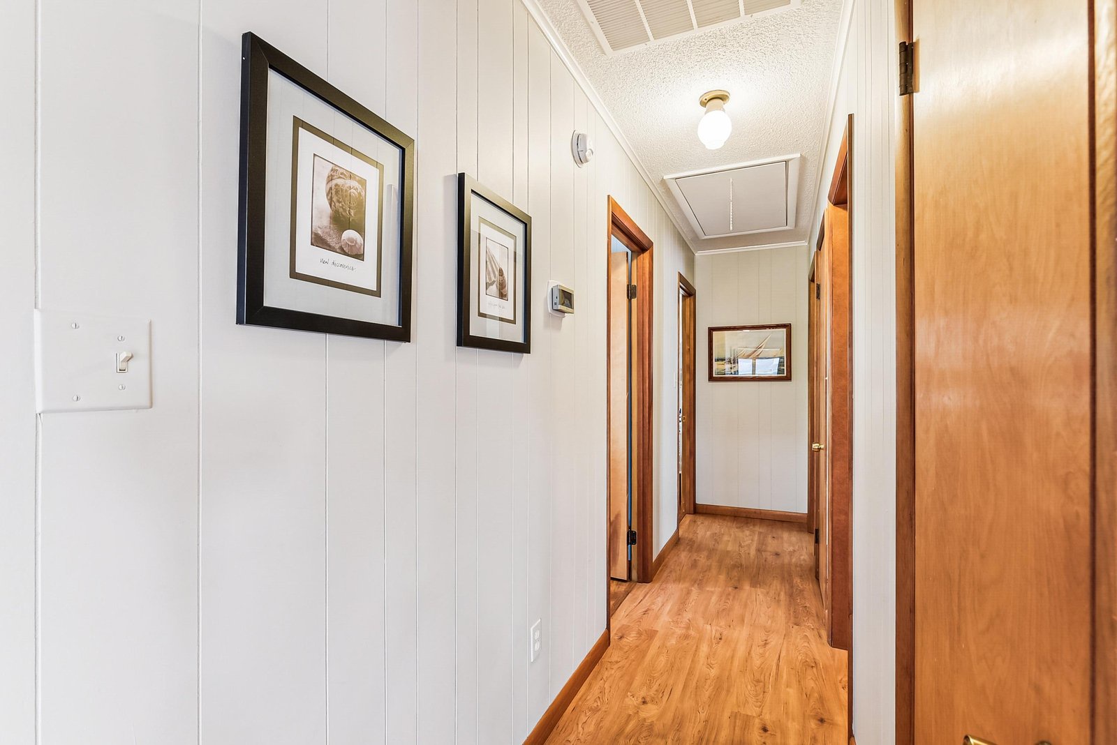 A welcoming hallway connects your private spaces, with warm wood floors, bright lighting, and coastal-inspired artwork setting a relaxed, home-away-from-home vibe.