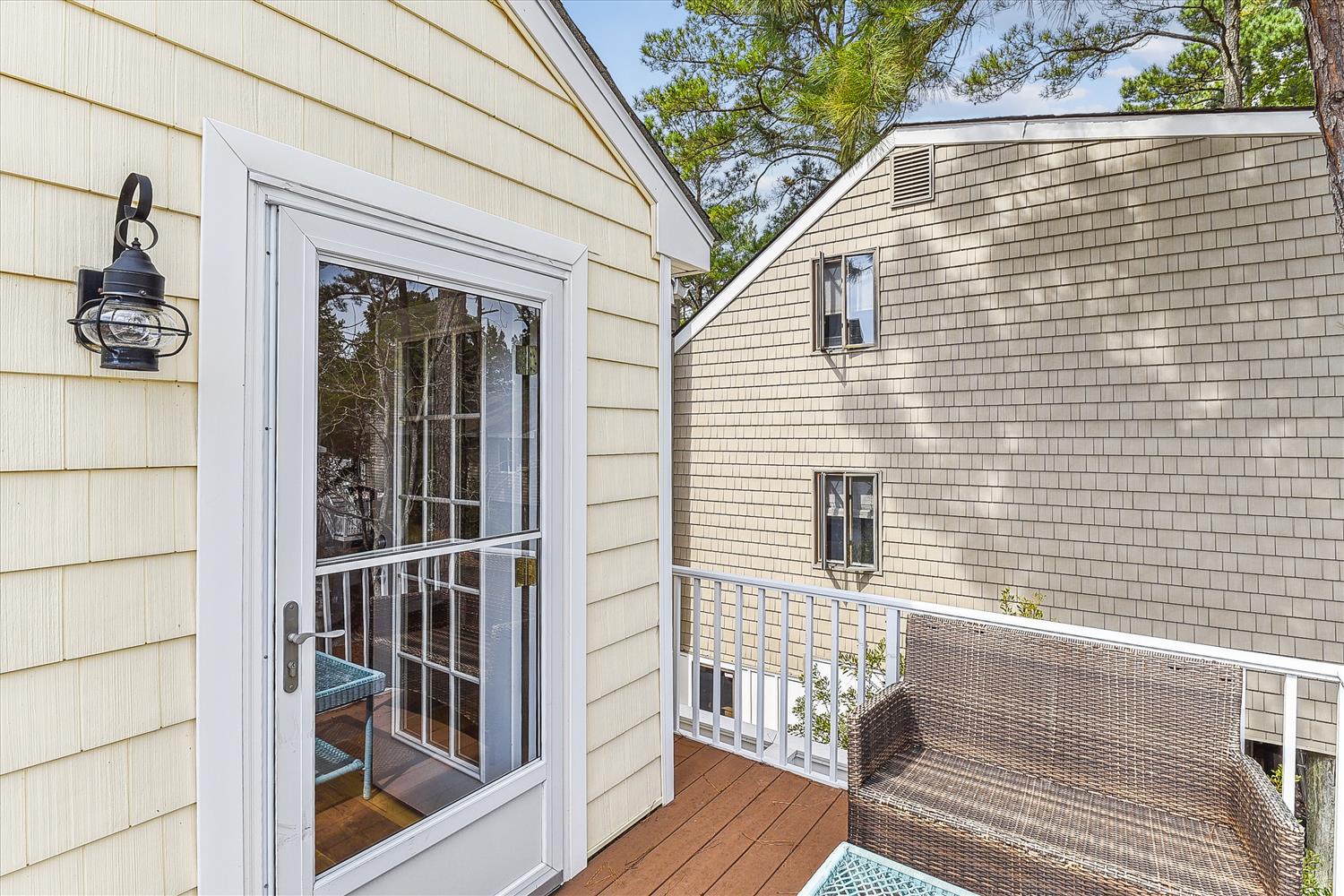 A private balcony with inviting wicker seating framed by coastal lantern lighting and views of the surrounding treetops.