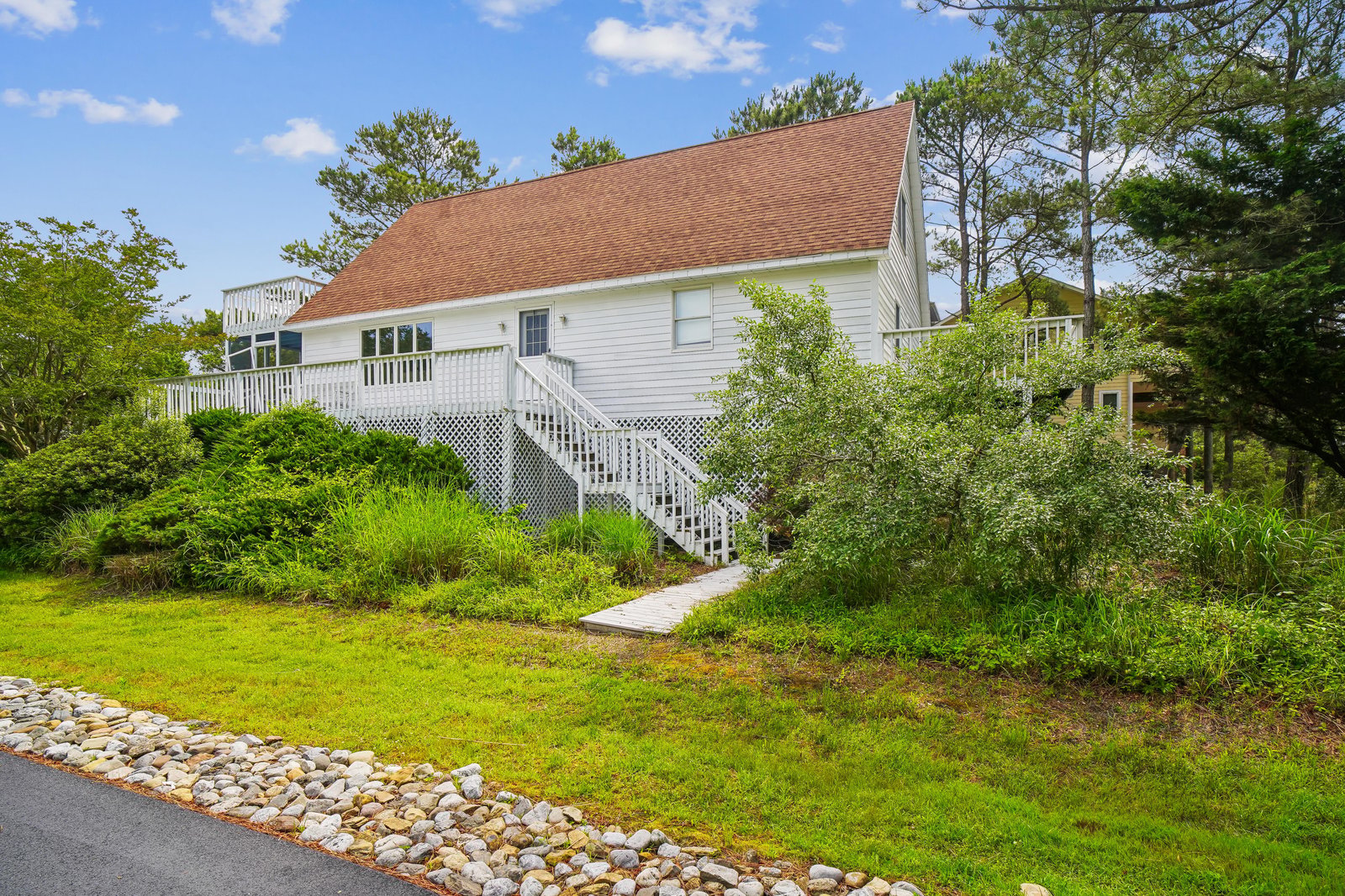 A classic white-sided coastal cottage with charming red roof, nestled among lush greenery and tall pines, offering a peaceful retreat surrounded by natural beauty.