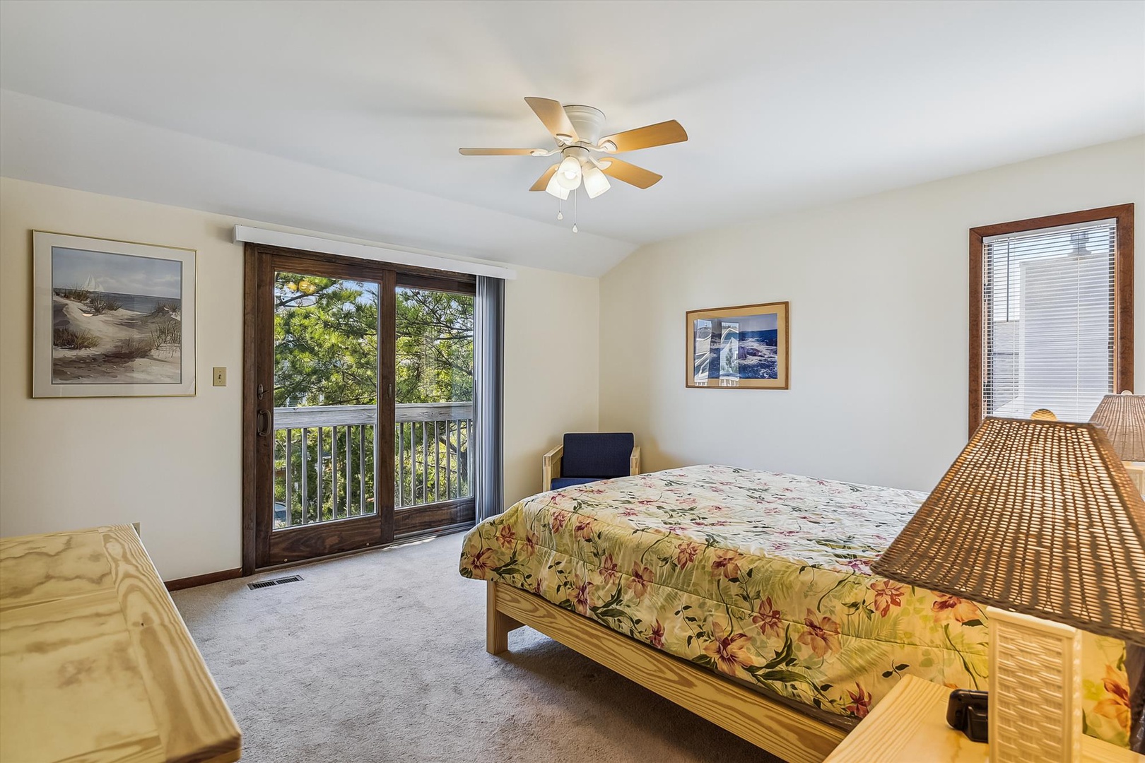 Your bright bedroom offers peaceful tree views through sliding glass doors, a ceiling fan to keep you comfortable, and cheerful coastal artwork that sets a relaxed, beachy tone.