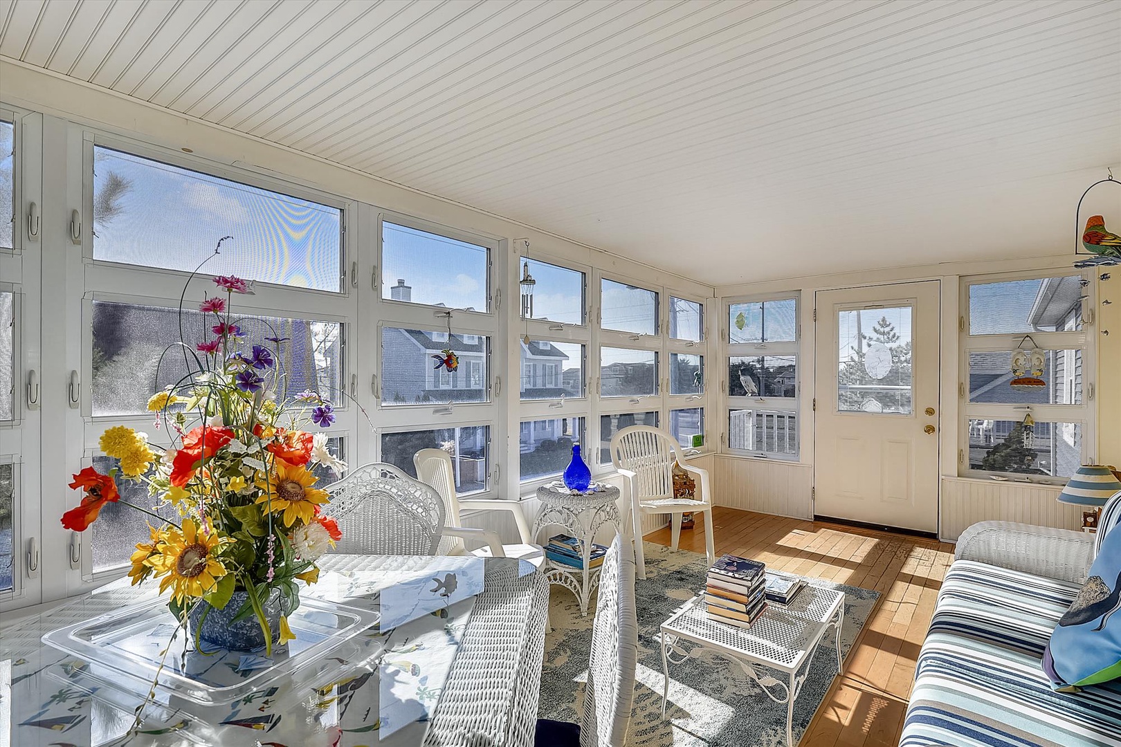Bright sunroom with white wicker seating, fresh flowers, and panoramic windows inviting natural light into your peaceful retreat.