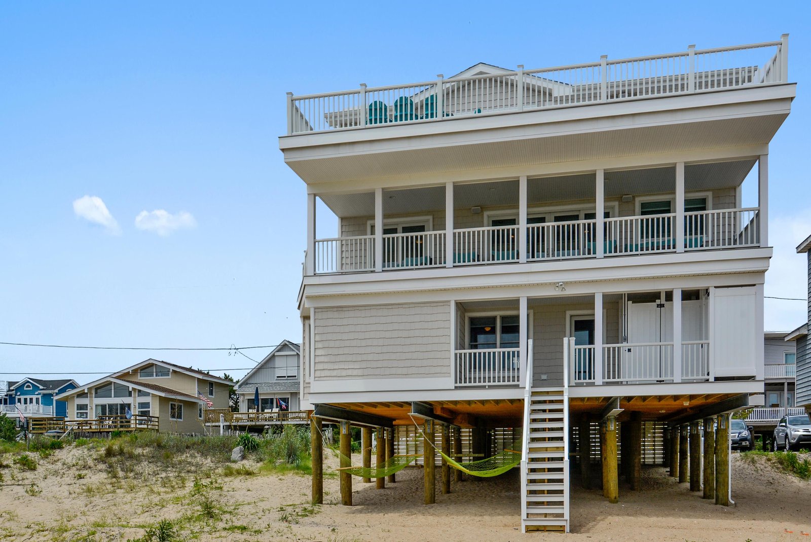 A multi-level beachfront property showcasing stilt construction for coastal resilience, with spacious covered porches, a rooftop deck, and direct beach access in a relaxed oceanside neighborhood.