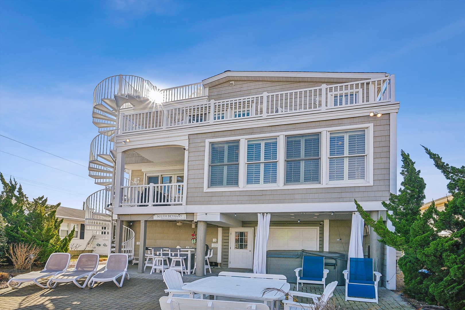 This beachside property features a distinctive spiral staircase to the upper deck, spacious outdoor lounging areas, and coastal-inspired architecture situated in a quiet residential setting.