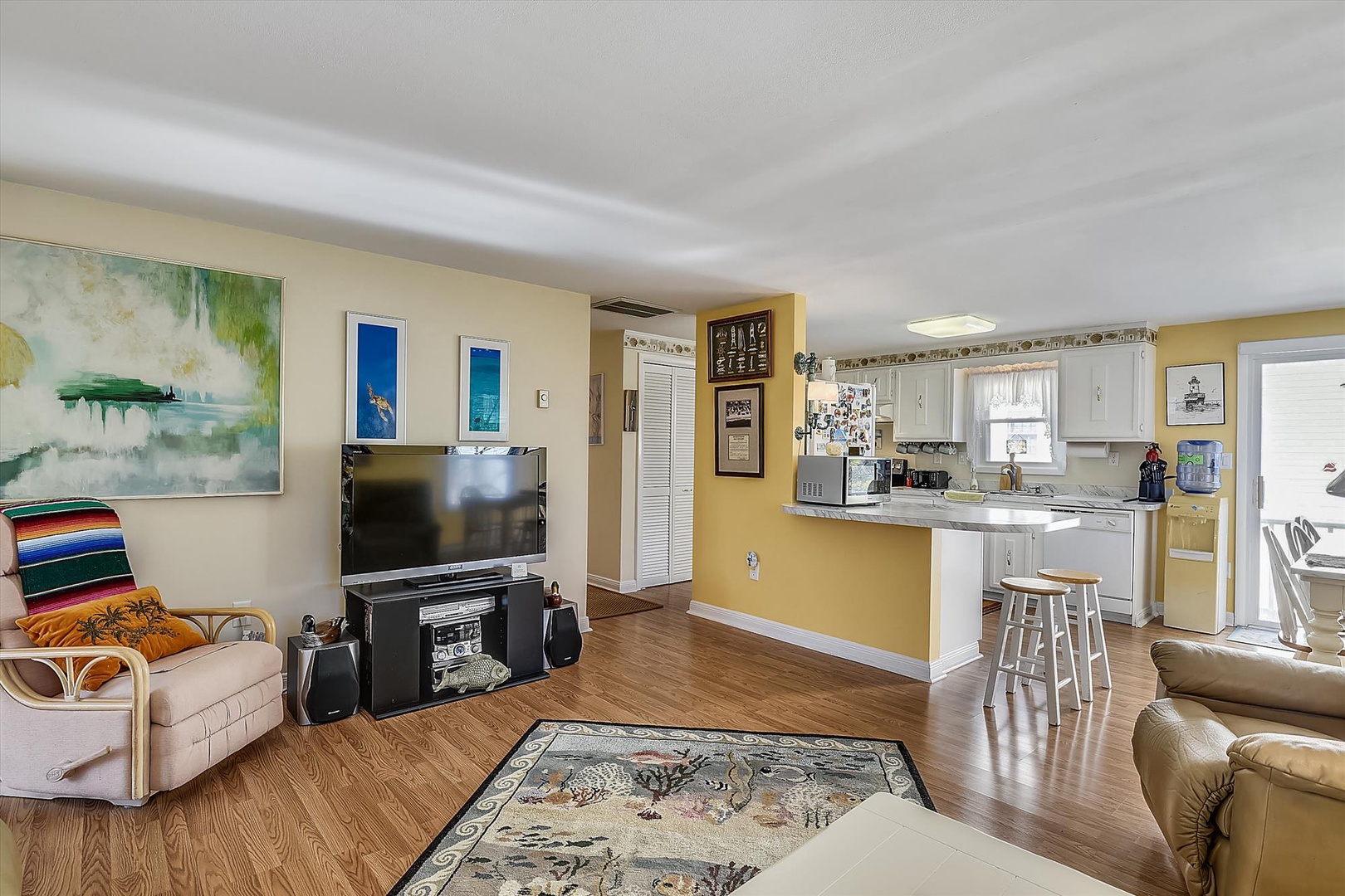 Open and inviting living space flows seamlessly into the kitchen, perfect for relaxing with family or preparing meals together. Bright coastal artwork and warm tones create a welcoming atmosphere.